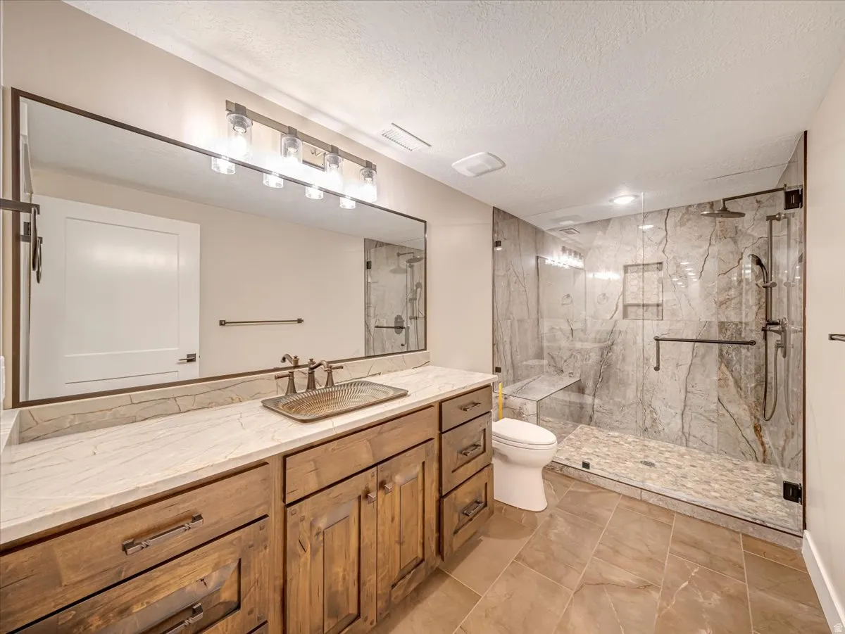 Spacious bathroom featuring a large walk-in shower with stone tile walls and a pebble floor, a dual-head shower system, and a built-in shower bench