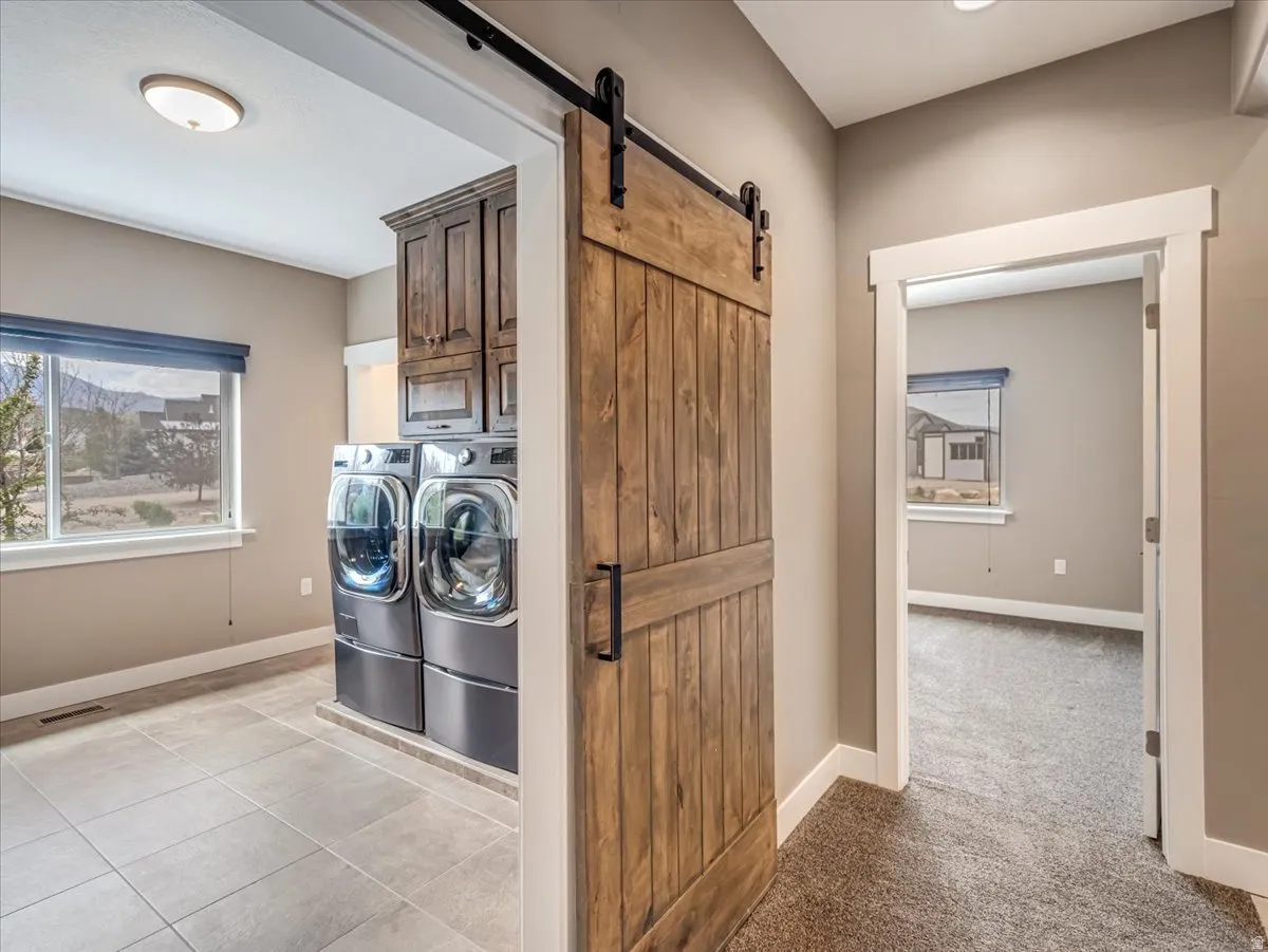 Laundry area featuring a rustic wood barn door, upper cabinetry, tile flooring, and a large window
