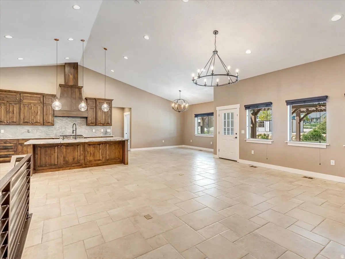 Open-concept living area featuring a vaulted ceiling with recessed lighting, large format tile flooring, and a contemporary chandelier