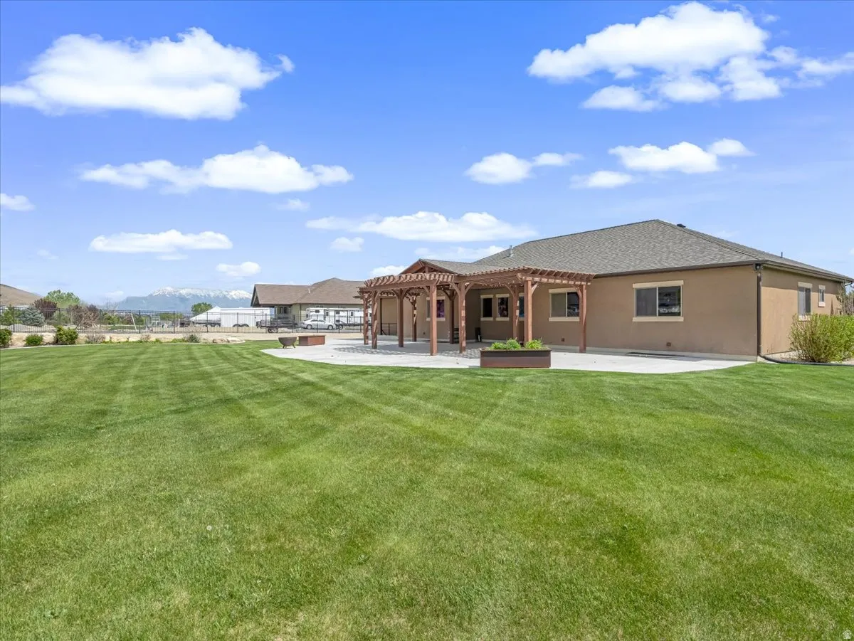 Expansive backyard featuring a large manicured lawn, a concrete patio, and a wooden pergola structure
