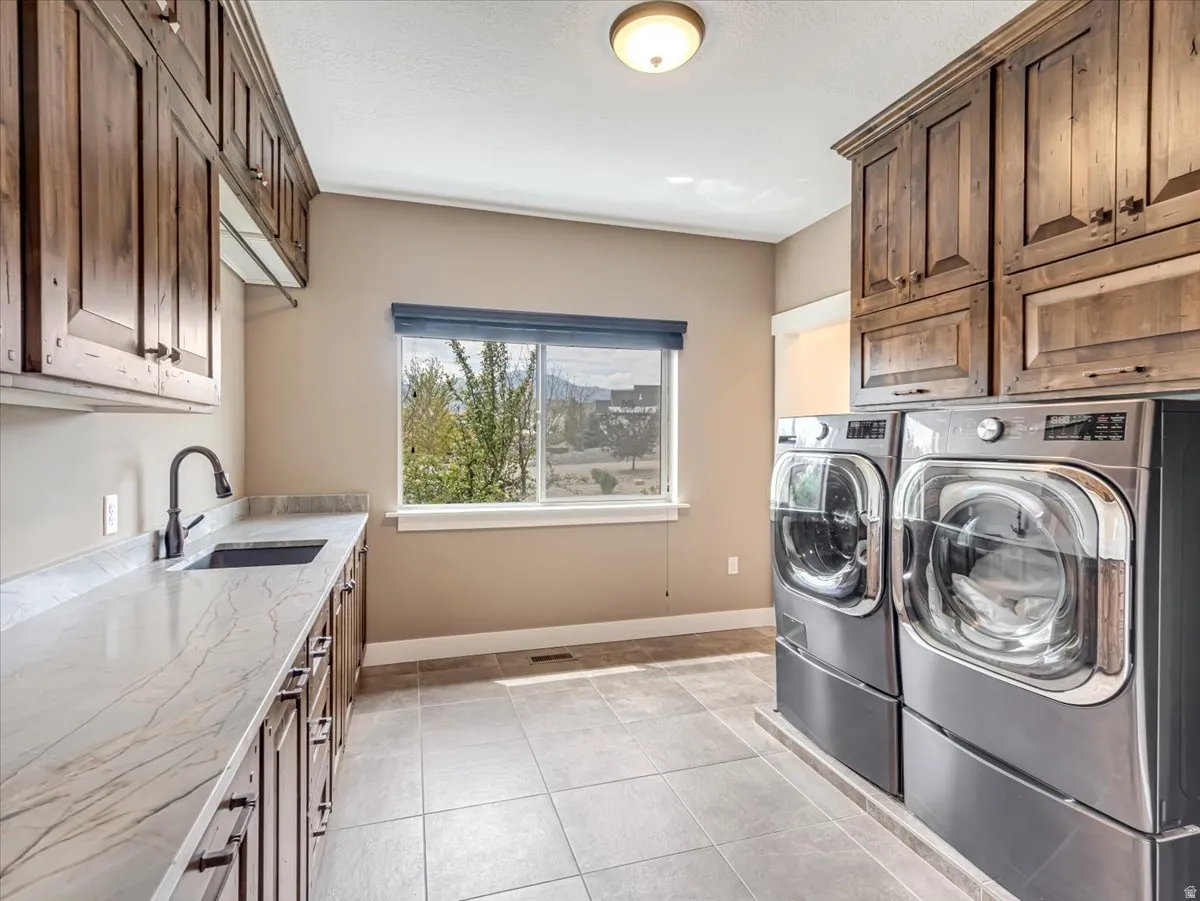 Utility room featuring ample cabinetry, a built-in sink with a gooseneck faucet, light-toned countertops, and large format floor tiling