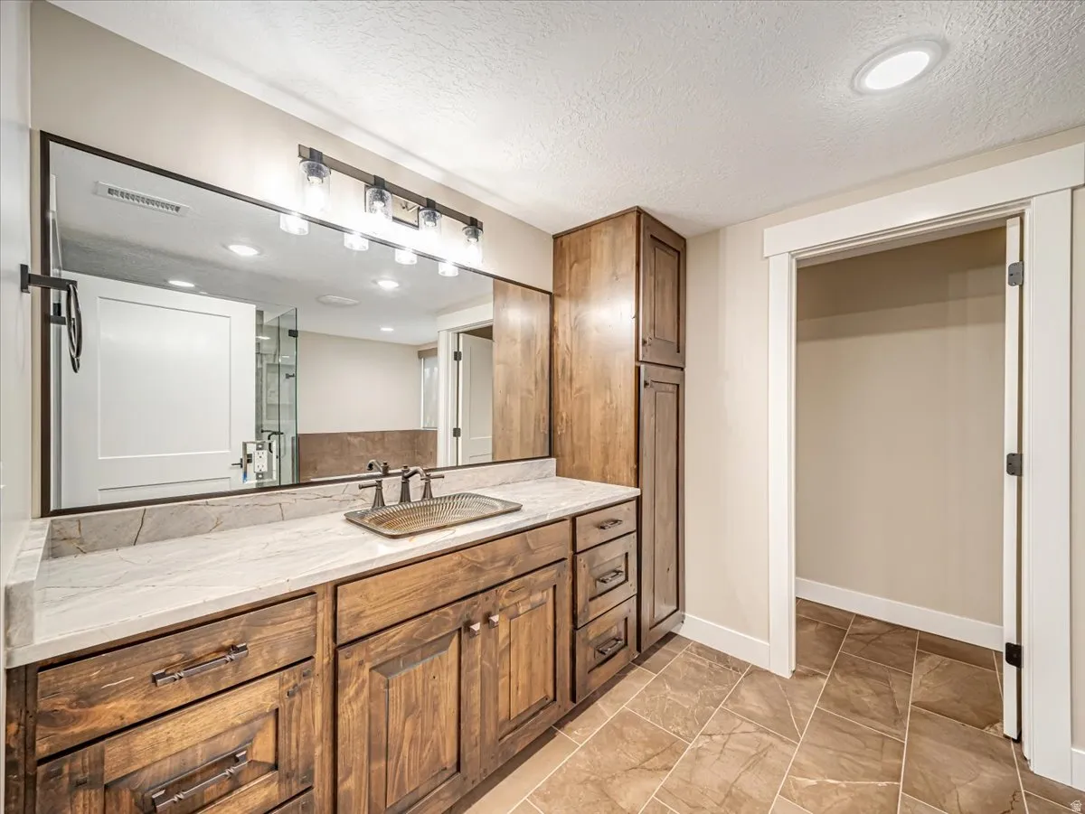 Vanity featuring wood cabinetry with ample storage, a light-toned countertop, and a large mirror with overhead lighting