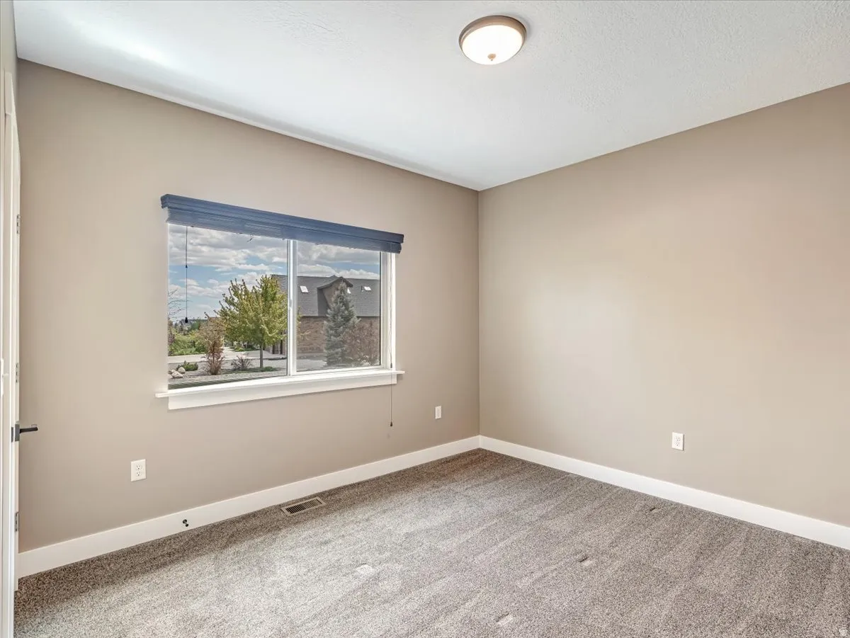 Carpeted room featuring a large window with white trim, a recessed floor vent, and a flush mount ceiling light fixture
