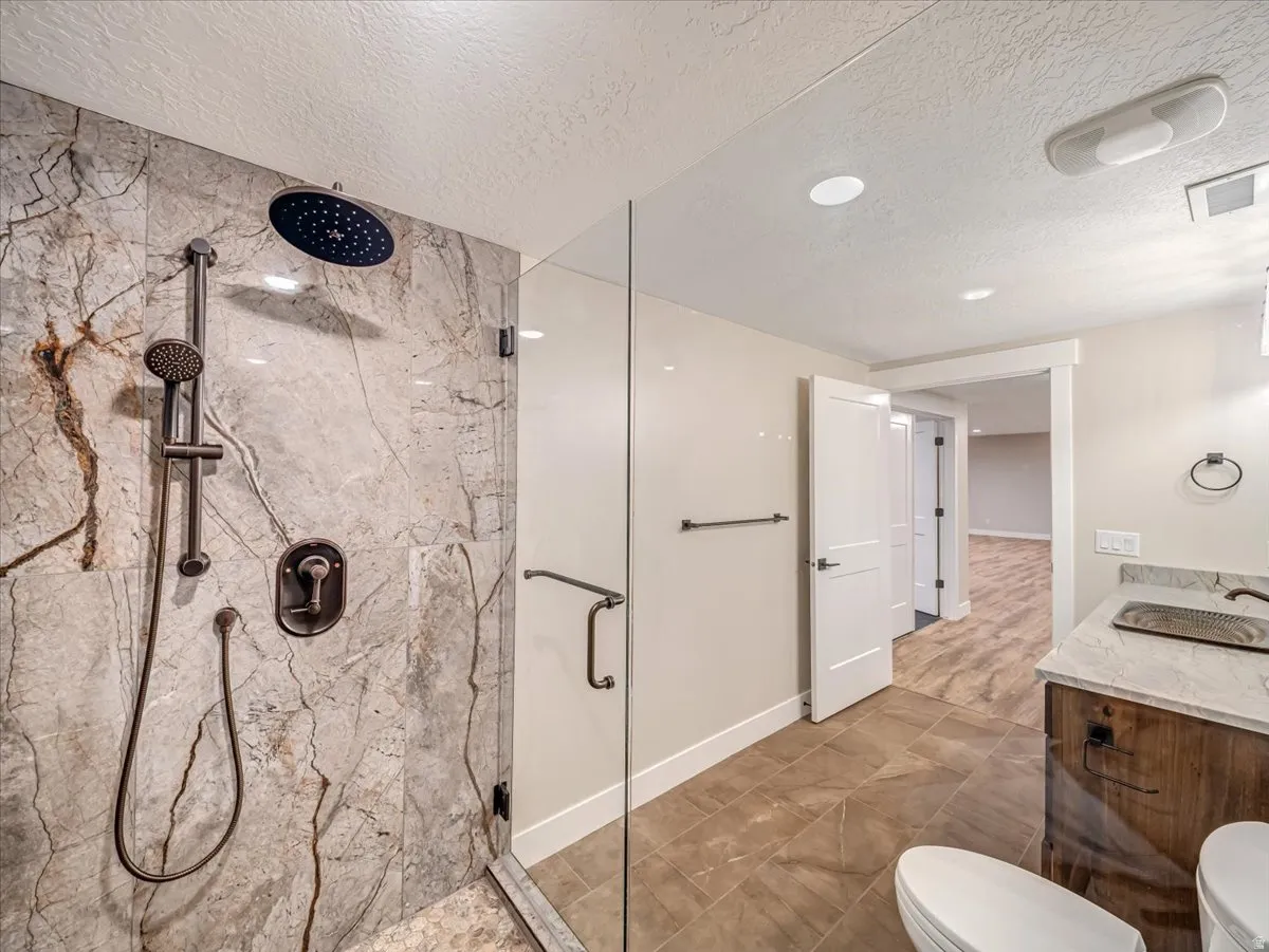 Walk-in shower featuring a rain shower head, handheld shower, and natural stone-look tile surround