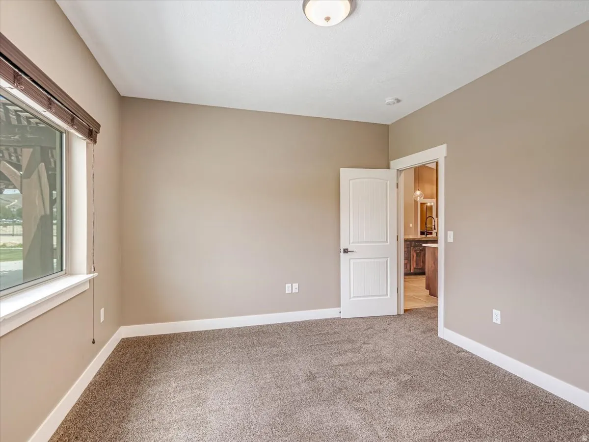 Neutral-toned room with plush carpet, a large window with blinds, and white trim