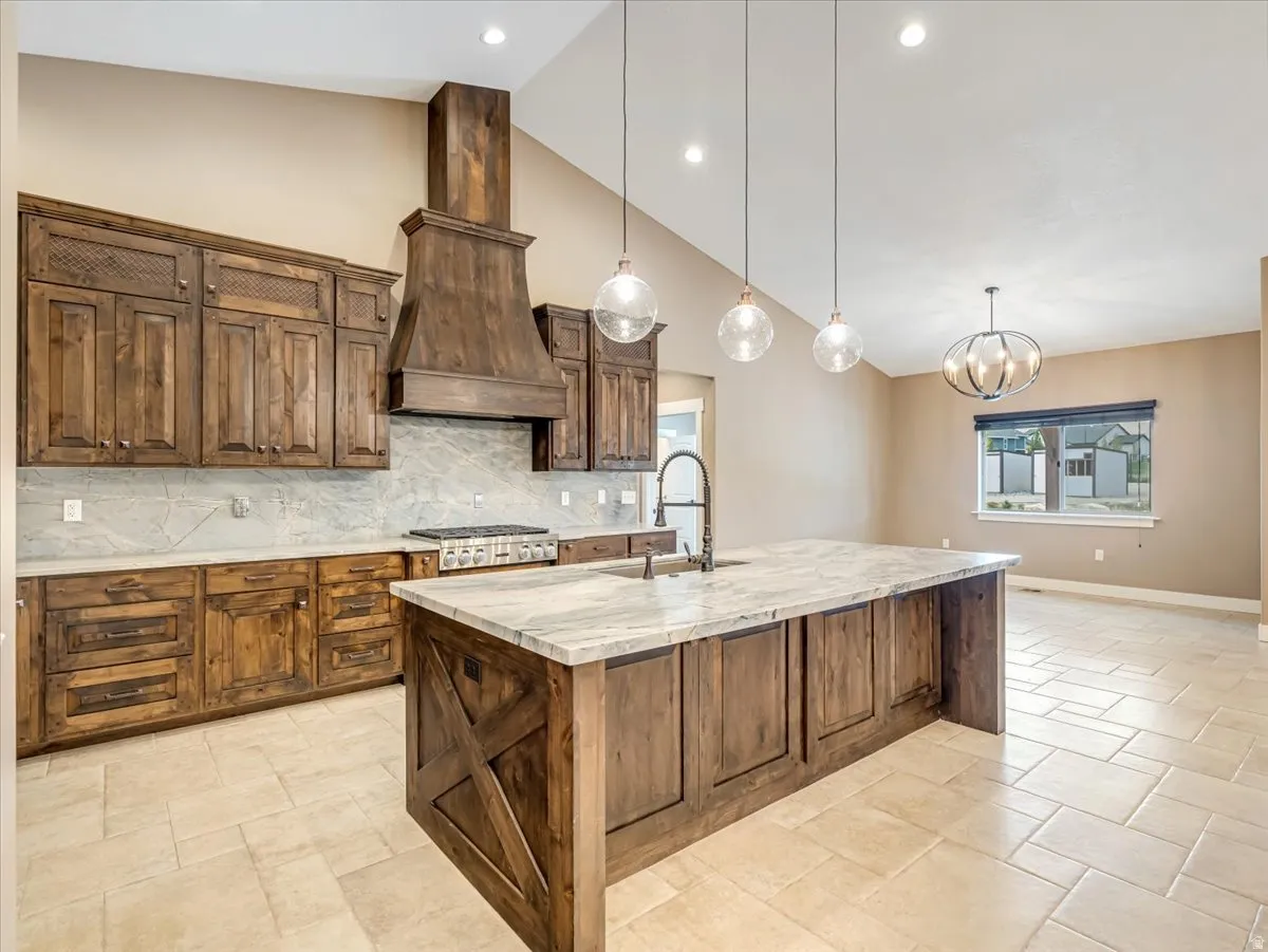 Kitchen featuring a substantial island with stone countertop, custom wood cabinetry, and a built-in range with a coordinating wood hood