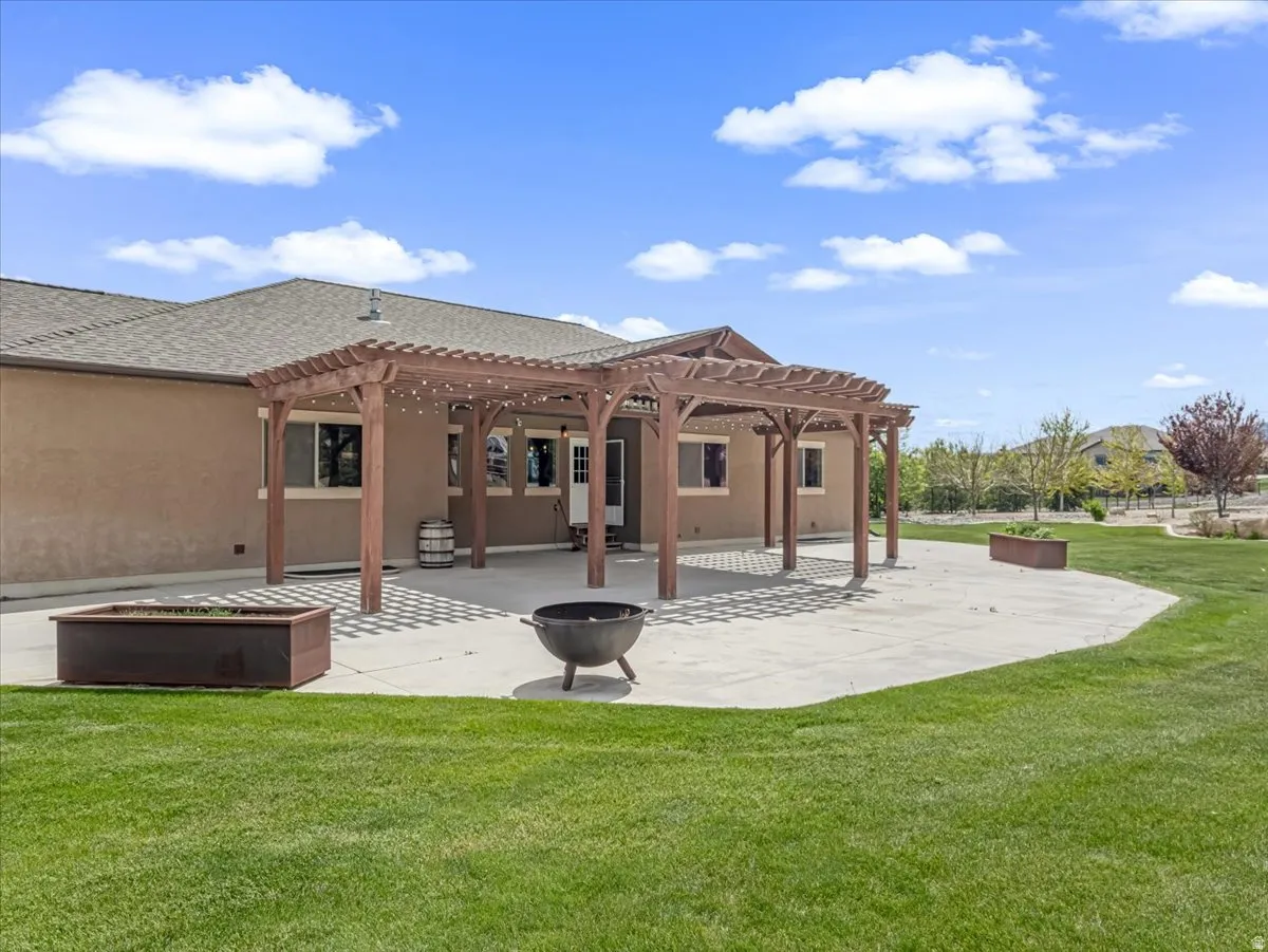 Spacious rear patio featuring a wooden pergola, concrete surfacing, and a manicured lawn area