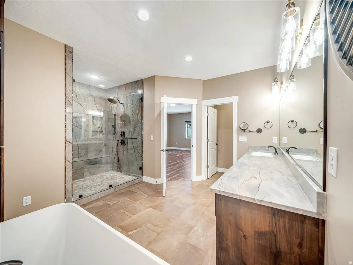 Spacious bathroom featuring a glass-enclosed shower with stone-look tile, a dual vanity with a patterned countertop, and a built-in soaking tub