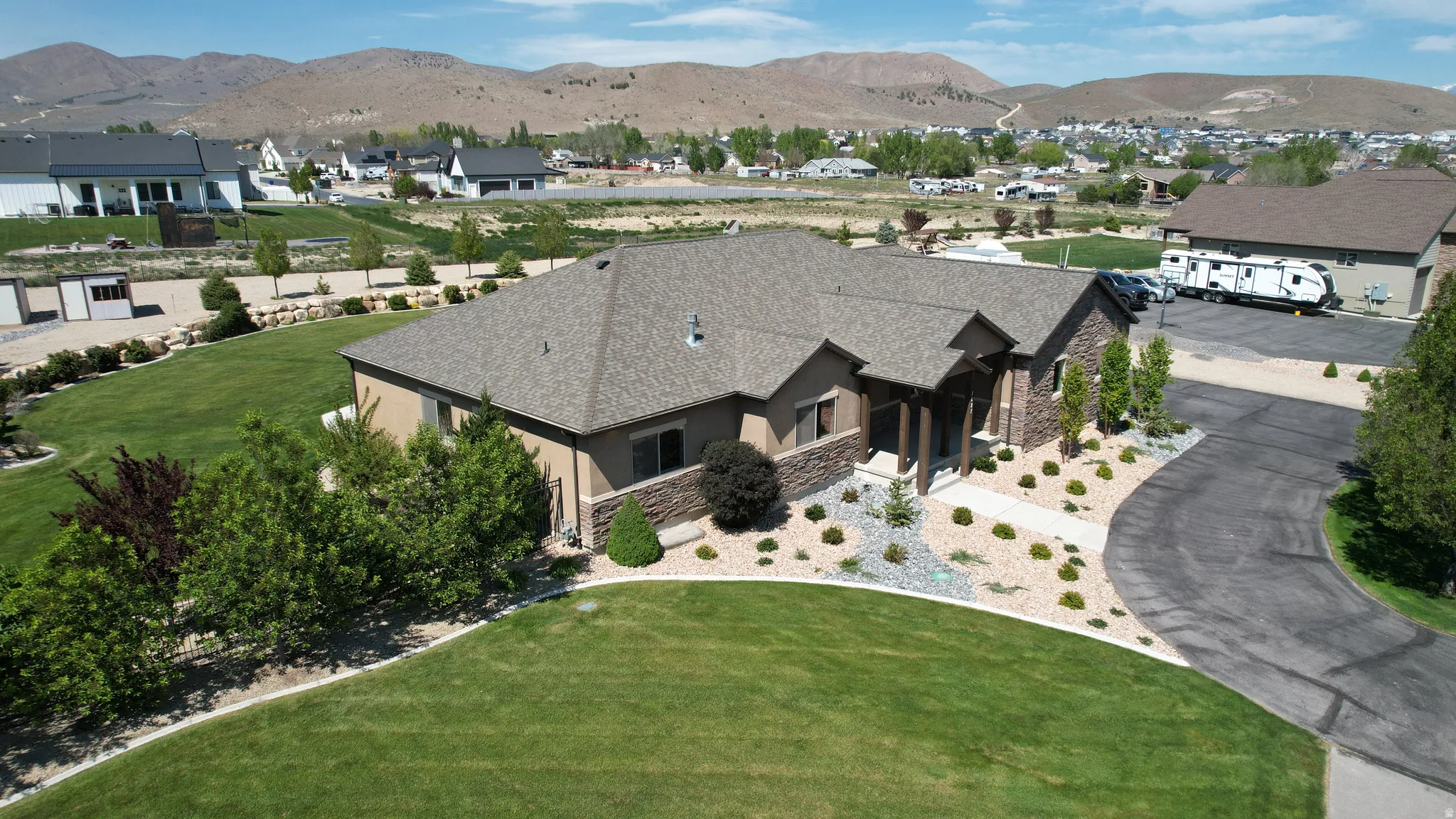 Ranch-style residence featuring a prominent stone facade, an attached two-car garage, and a expansive asphalt driveway