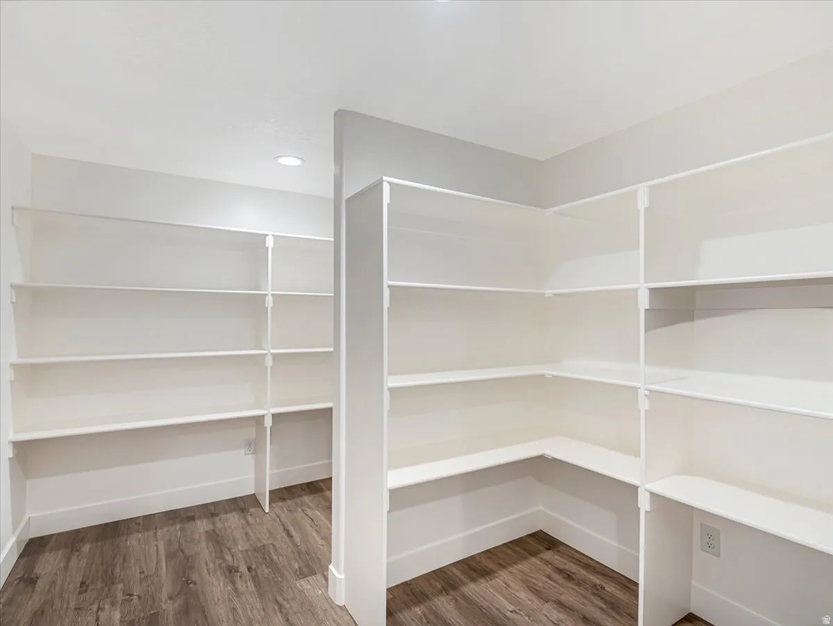 Spacious walk-in pantry featuring extensive white shelving, wood-finish flooring, recessed lighting, and crisp white trim