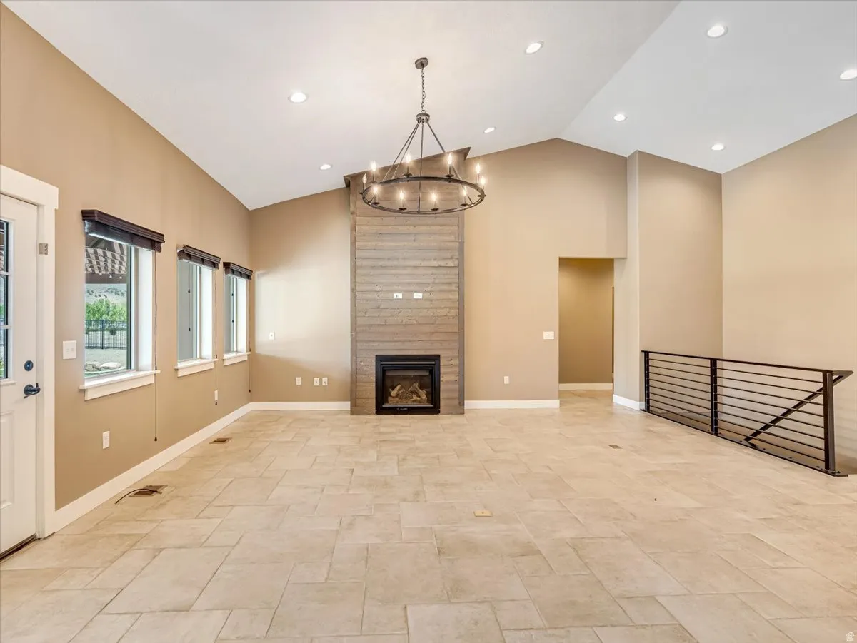 Spacious living area featuring a vaulted ceiling with recessed lighting, a contemporary chandelier, a fireplace with a stacked wood-finish surround, and large-format tile flooring