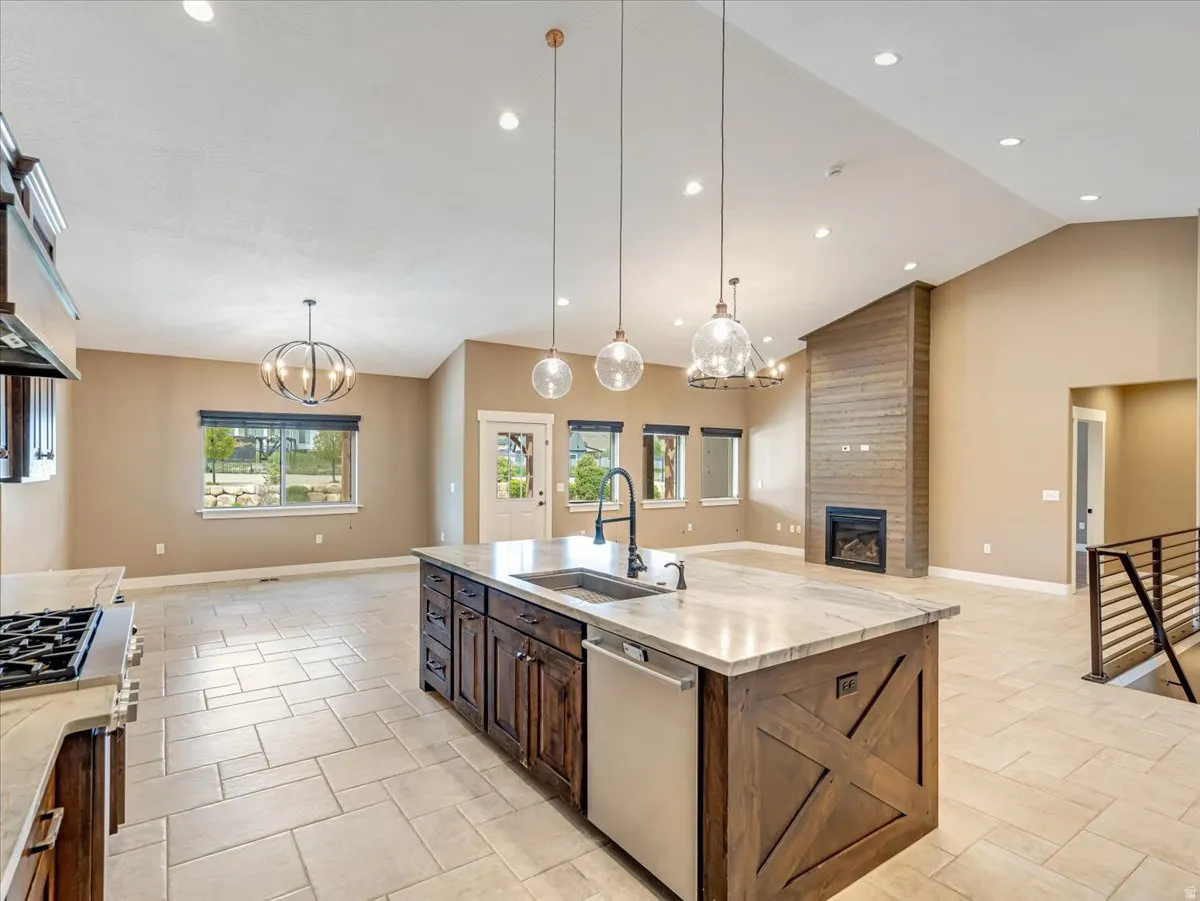 Open-concept living space featuring a central island with a sink and pendant lighting, a gas cooktop, tile flooring, a fireplace with a wood-finish accent wall, and multiple windows