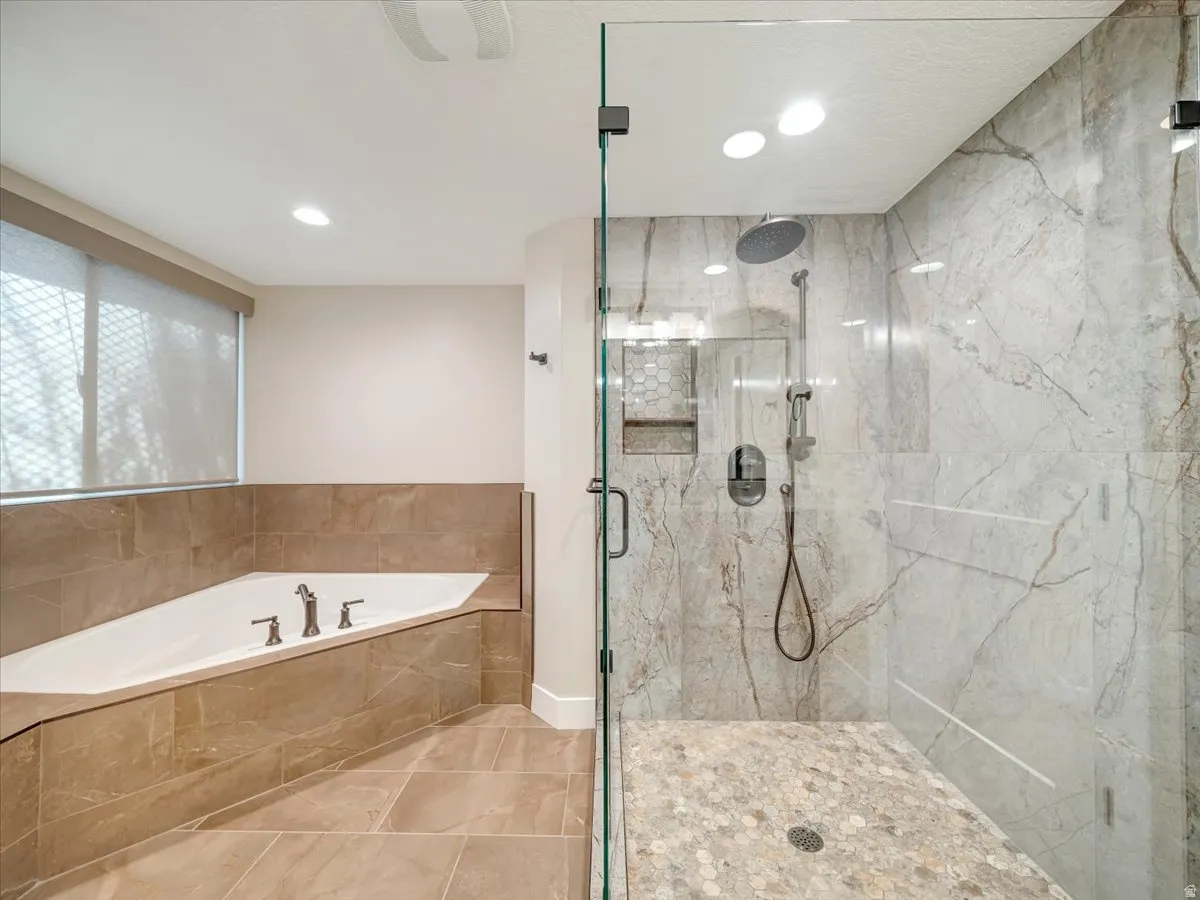 Spacious bathroom featuring a corner soaking tub, large glass-enclosed shower with pebble-tile floor, rain shower head, and full-height stone-look tile walls