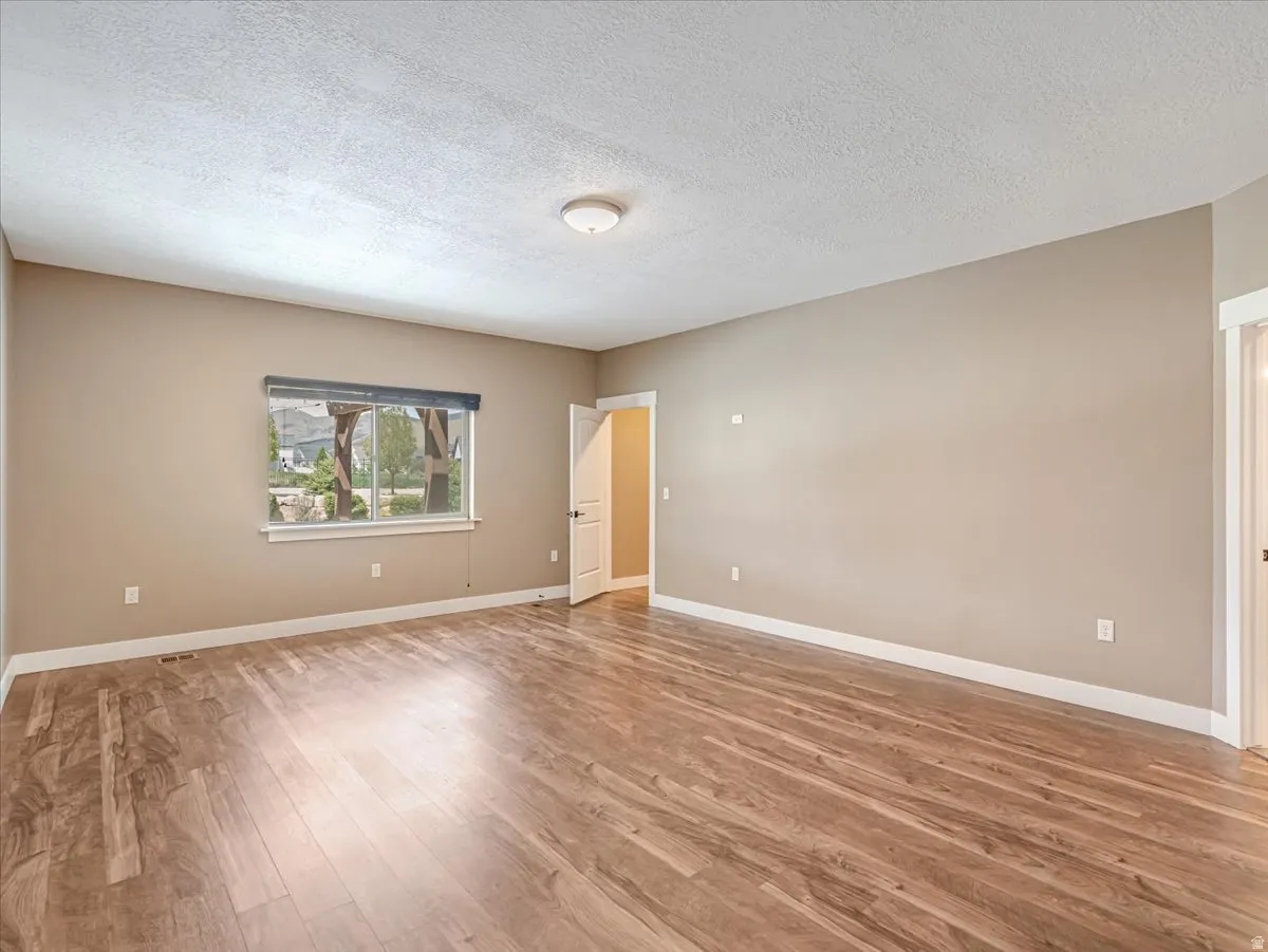 Spacious room featuring wood-finish flooring, neutral wall tones, a large window with roller shades, and white trim throughout
