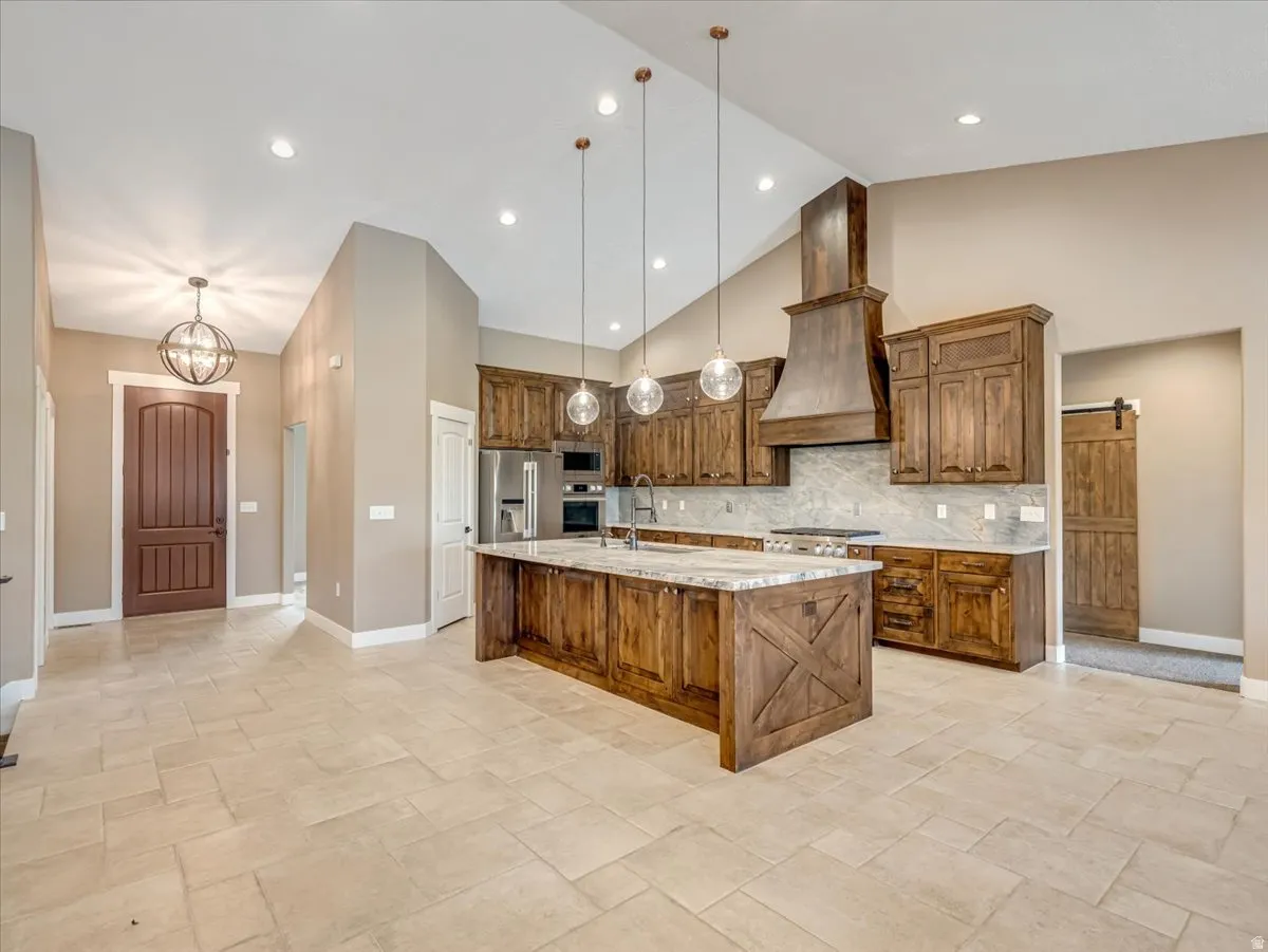 Spacious kitchen featuring an expansive center island with seating, a custom wood vent hood, and stainless steel appliances