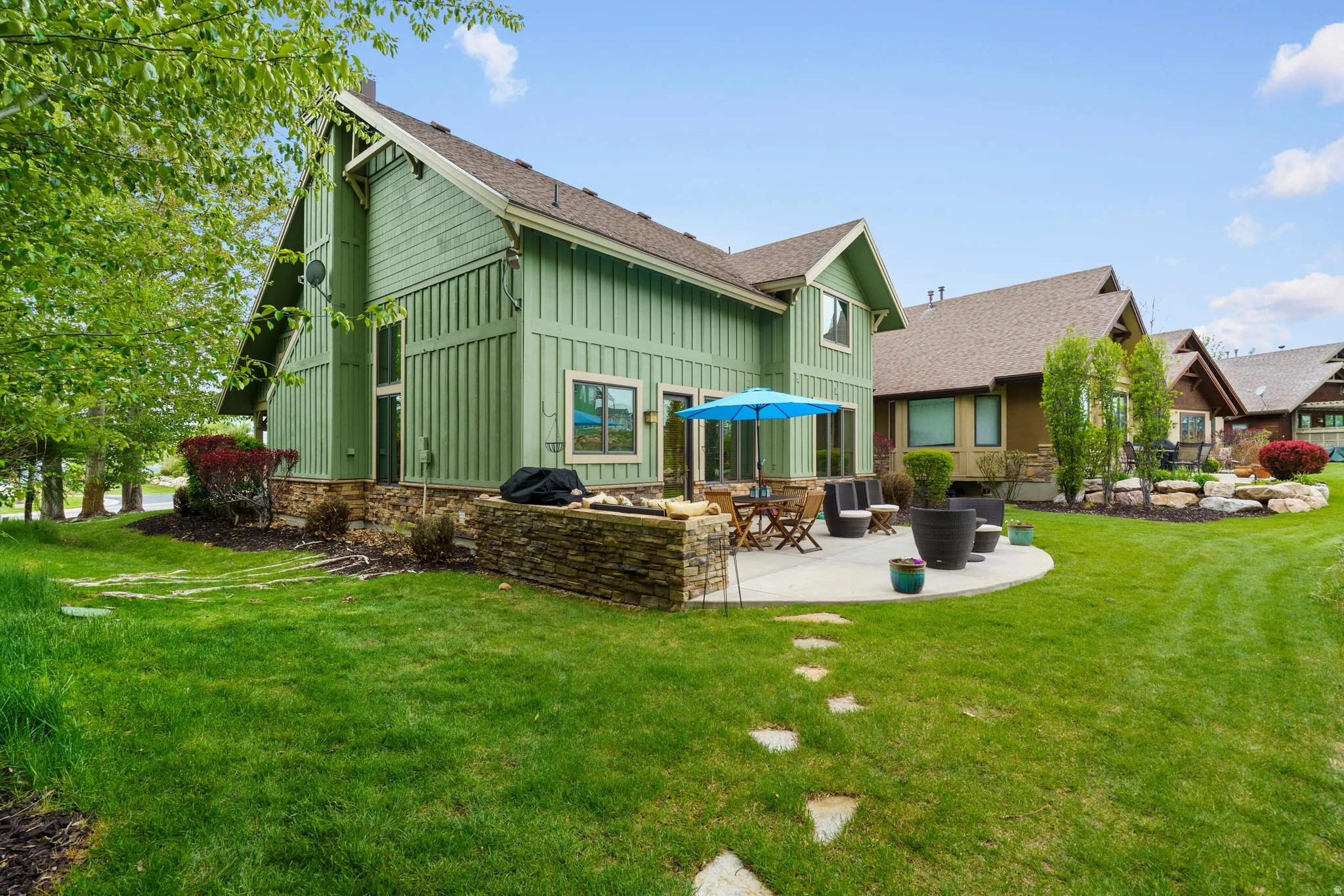 Expansive green lawn surrounds a curved concrete patio with a stone-clad retaining wall