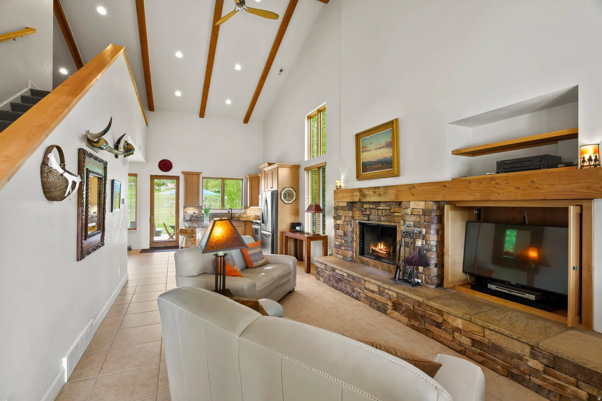Spacious living area featuring a vaulted ceiling with exposed wood beams, a stone fireplace, and a large built-in media cabinet