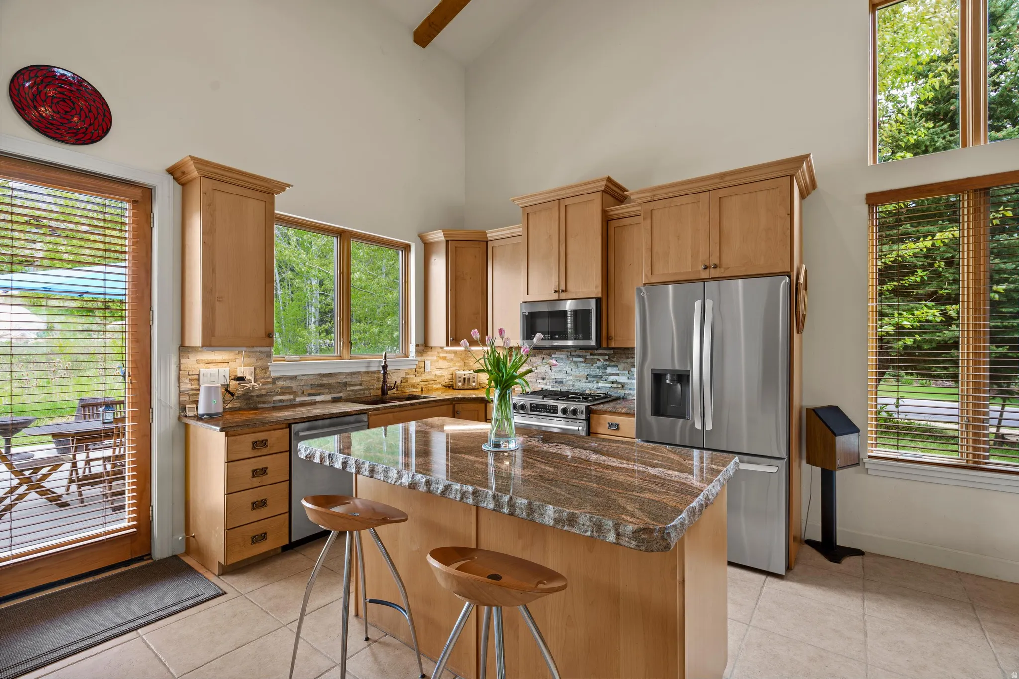 Kitchen featuring light wood cabinetry, stone-finish countertops, stainless steel appliances, and a central island with bar seating