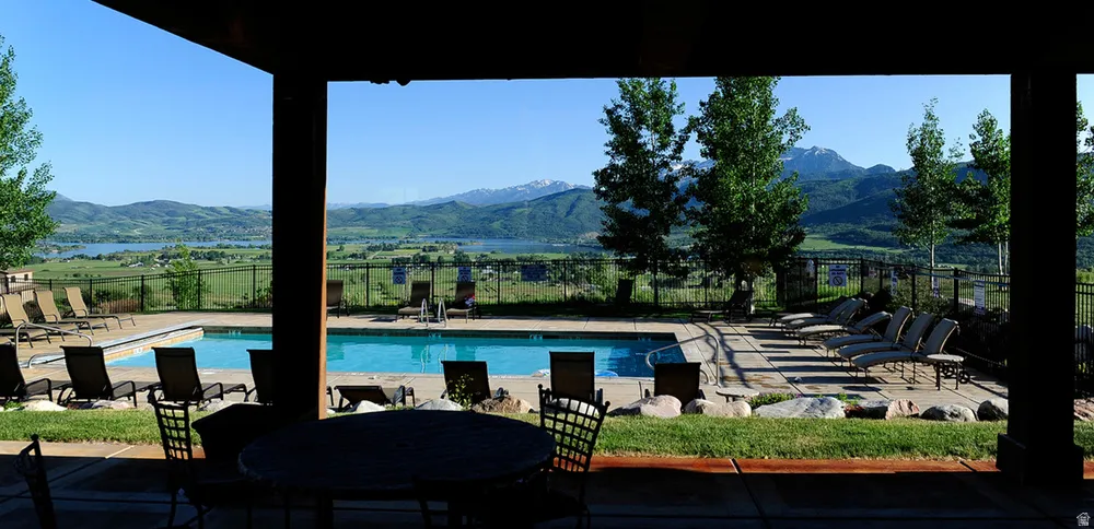 Outdoor swimming pool with surrounding concrete decking, a grassy perimeter, and a distant mountain and lake backdrop