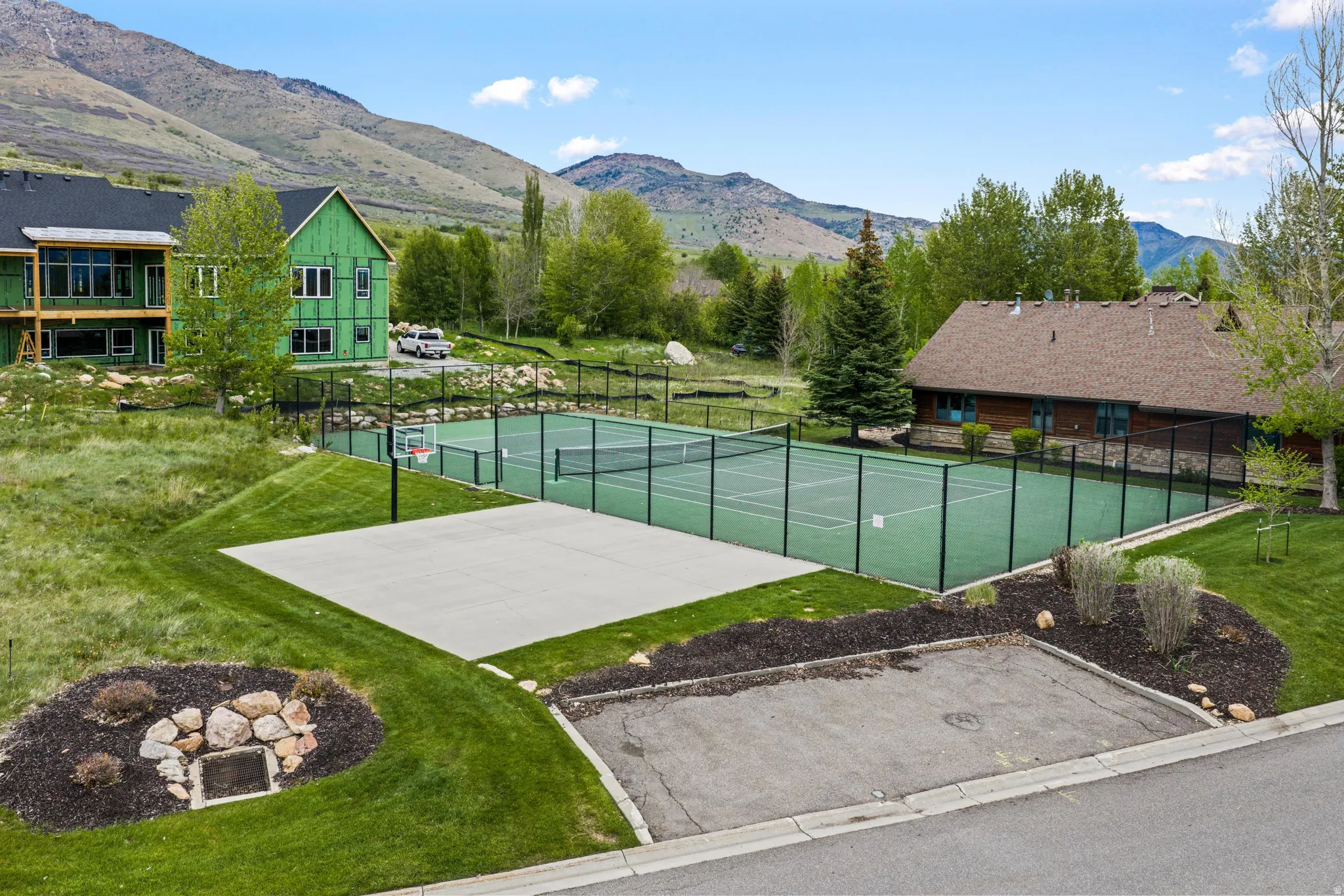 Outdoor sports court featuring a tennis court with black fencing and a concrete pad with a basketball hoop