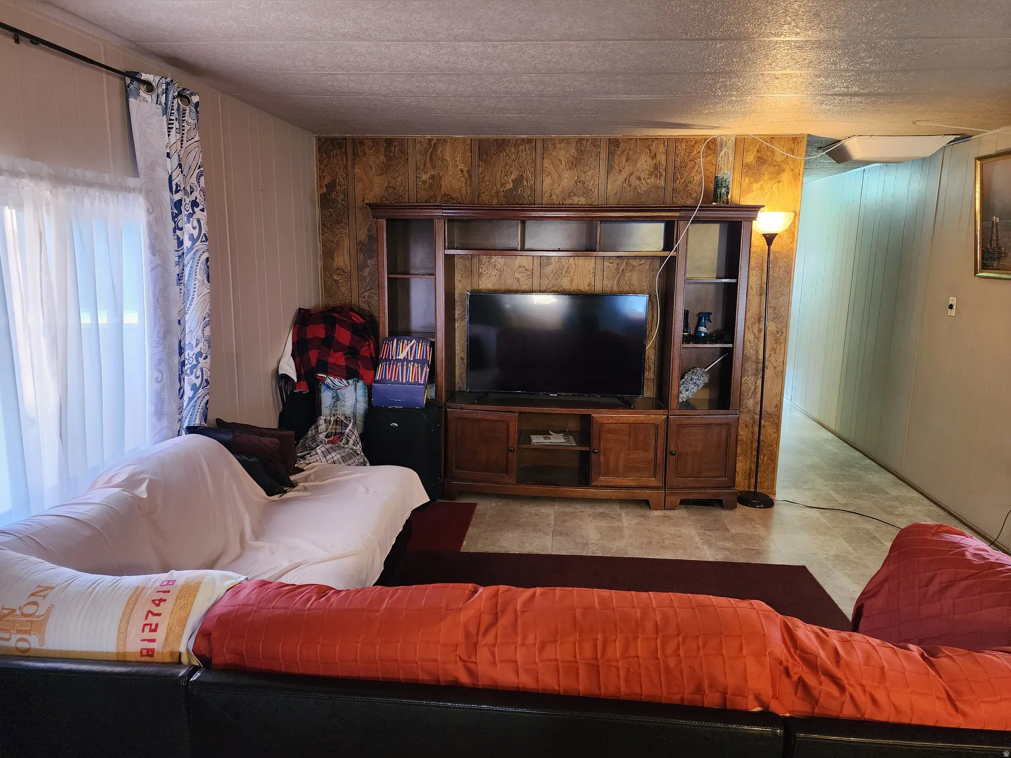 Living area featuring wood-finish wall paneling, sheet vinyl flooring, and a window with sheers