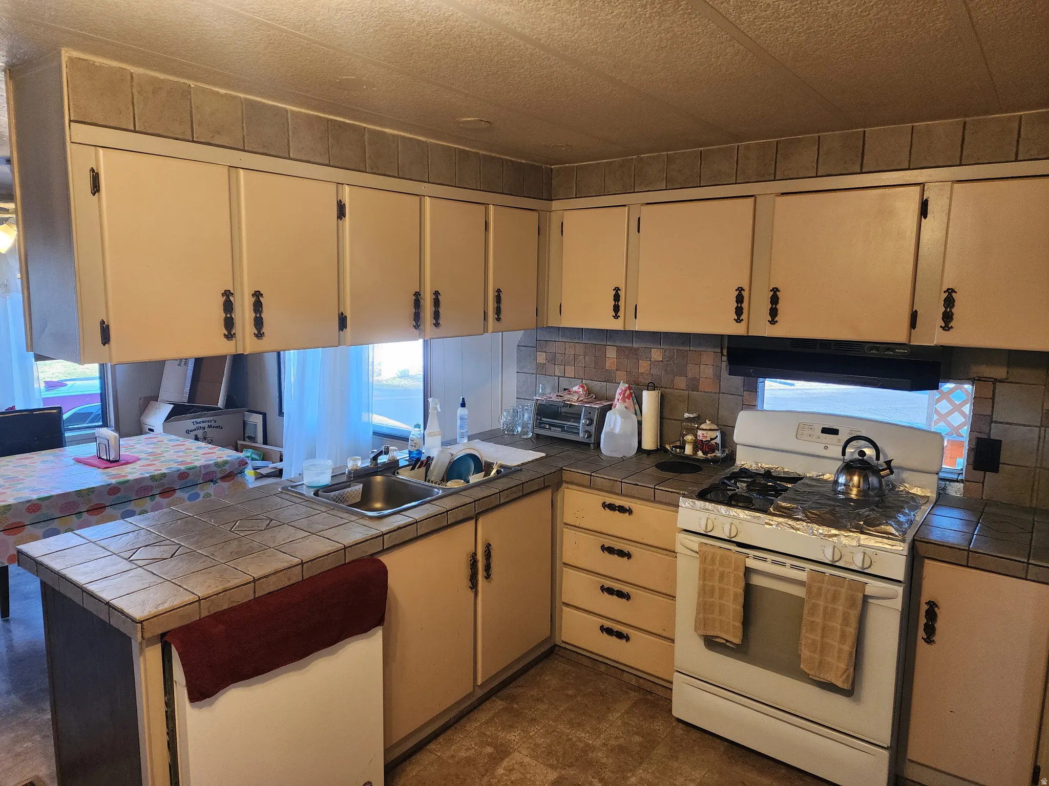 Functional kitchen featuring extensive cabinetry, tile countertops, a stainless steel sink, and a range with an overhead ventilation hood