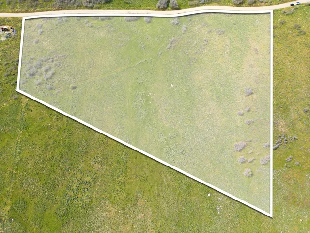 Expansive green lot featuring a distinct property boundary, varied ground cover, and a partial perimeter road