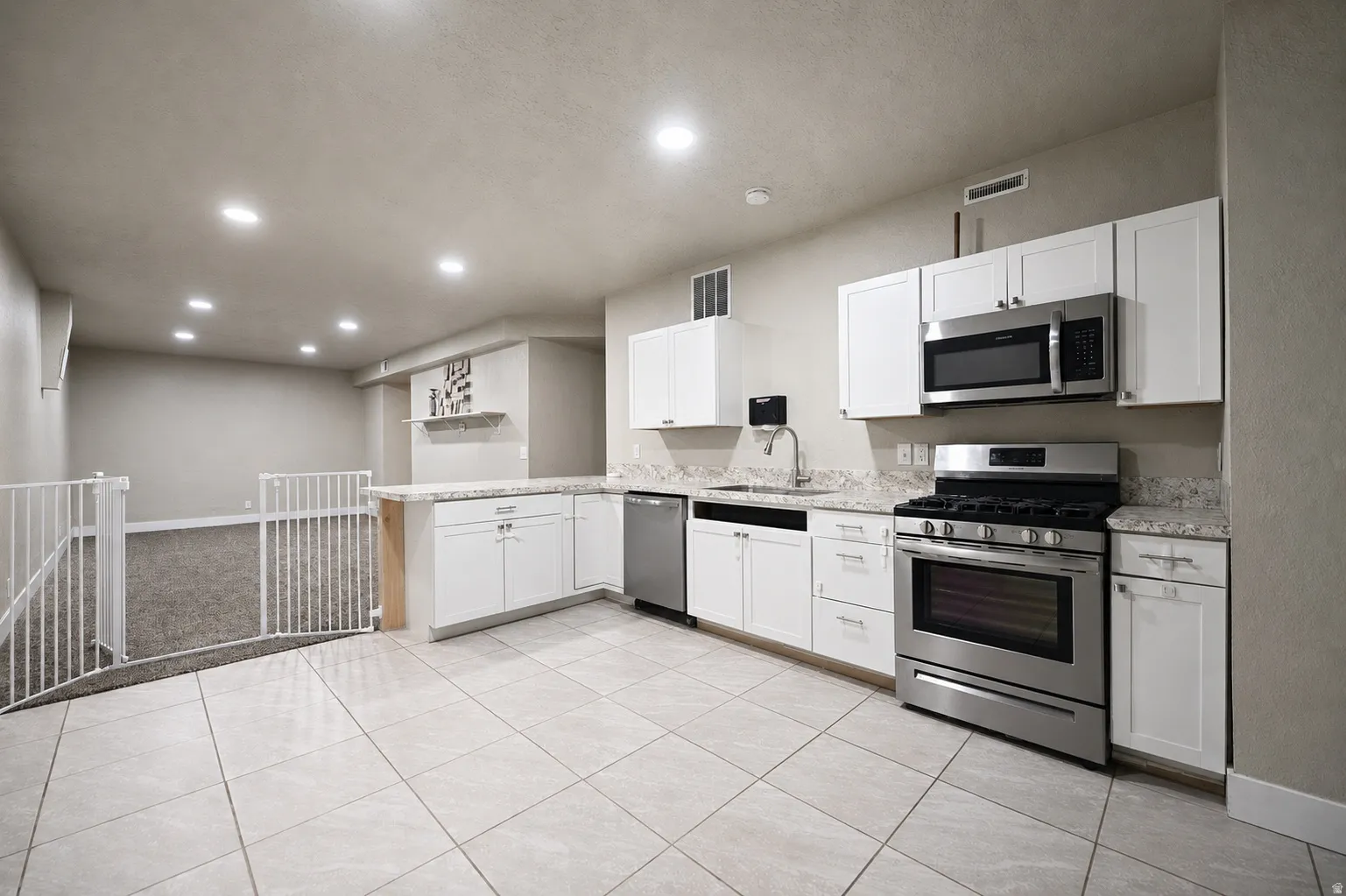 Kitchenette featuring white cabinetry, granite-style countertops, stainless steel appliances, and large format tile flooring