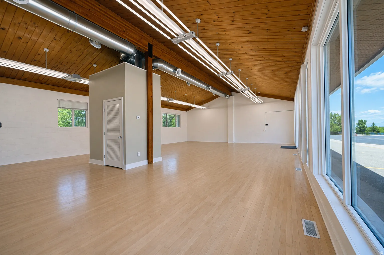 Spacious interior featuring a vaulted wood-paneled ceiling, exposed ductwork, extensive window line, neutral paint finishes, and light wood-finish flooring