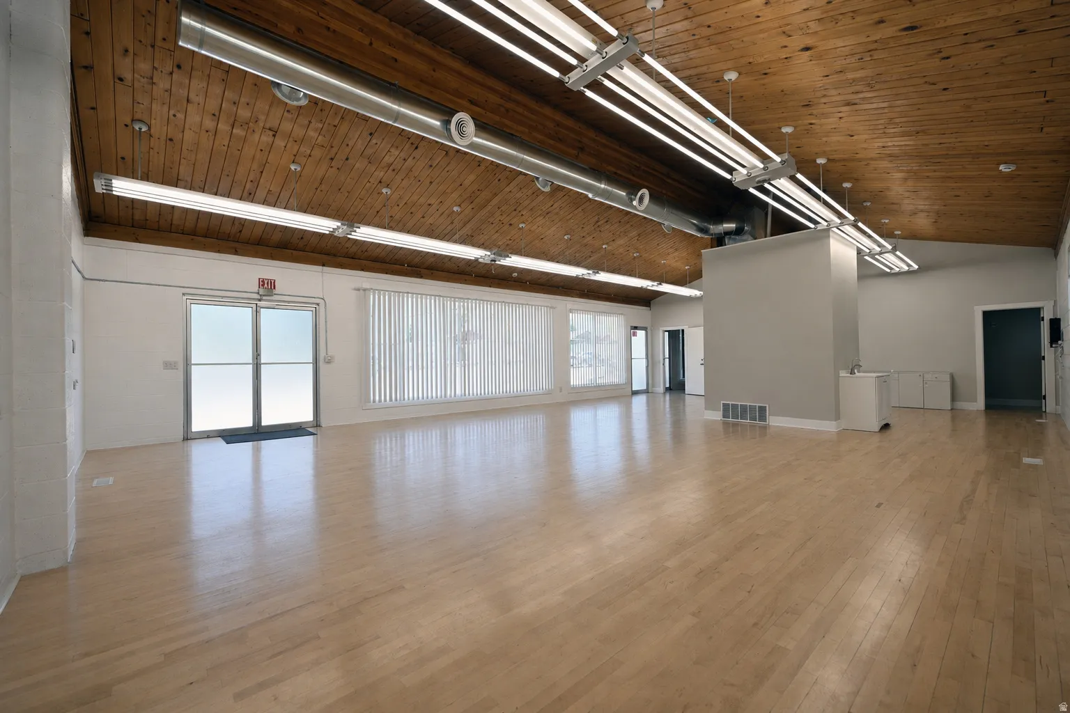 Spacious interior featuring a vaulted wood plank ceiling, light wood-finish flooring, and multiple fluorescent lighting fixtures