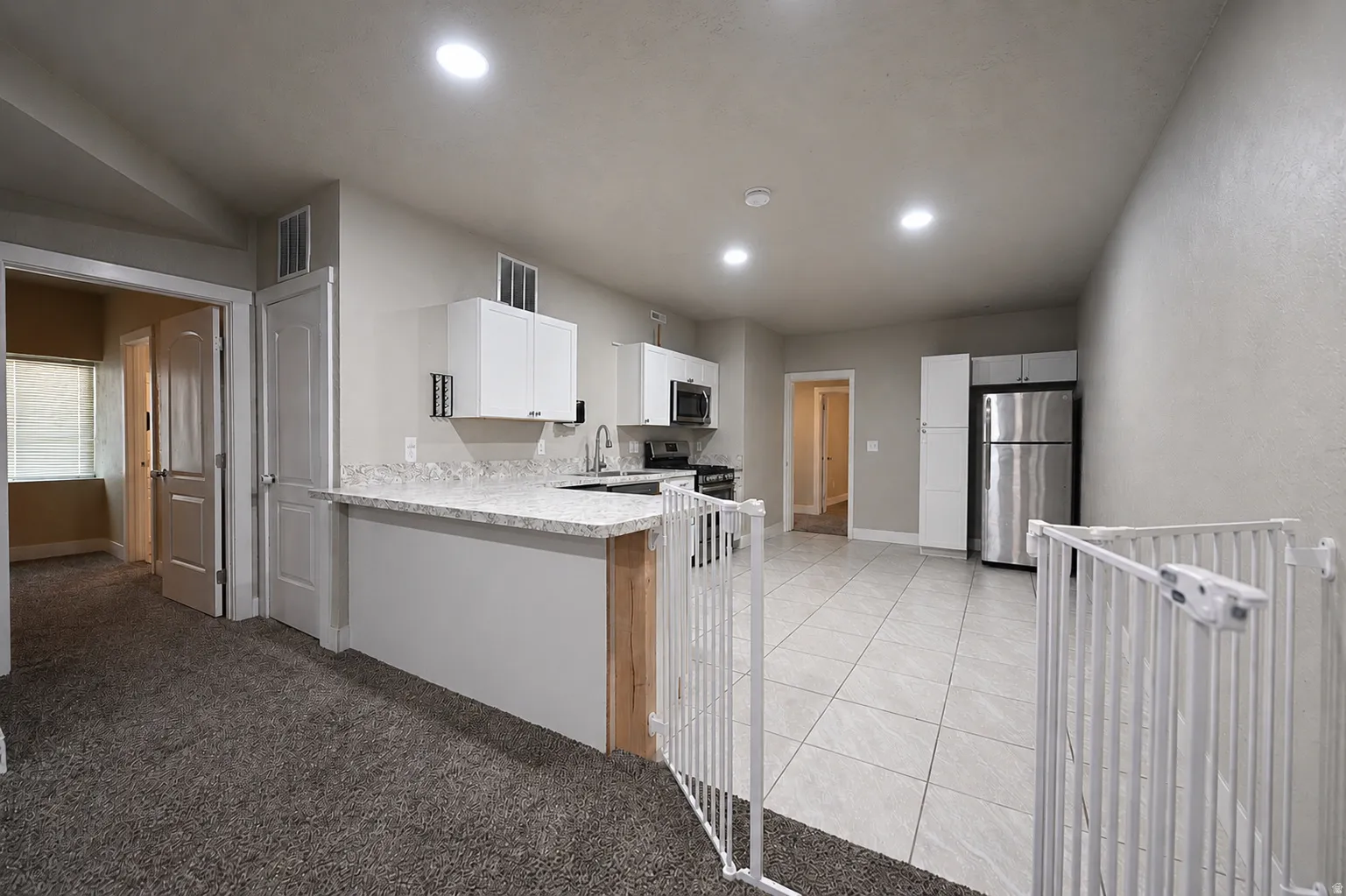 Open-concept kitchen and living area featuring white cabinetry, stainless steel appliances, speckled countertops, and recessed lighting
