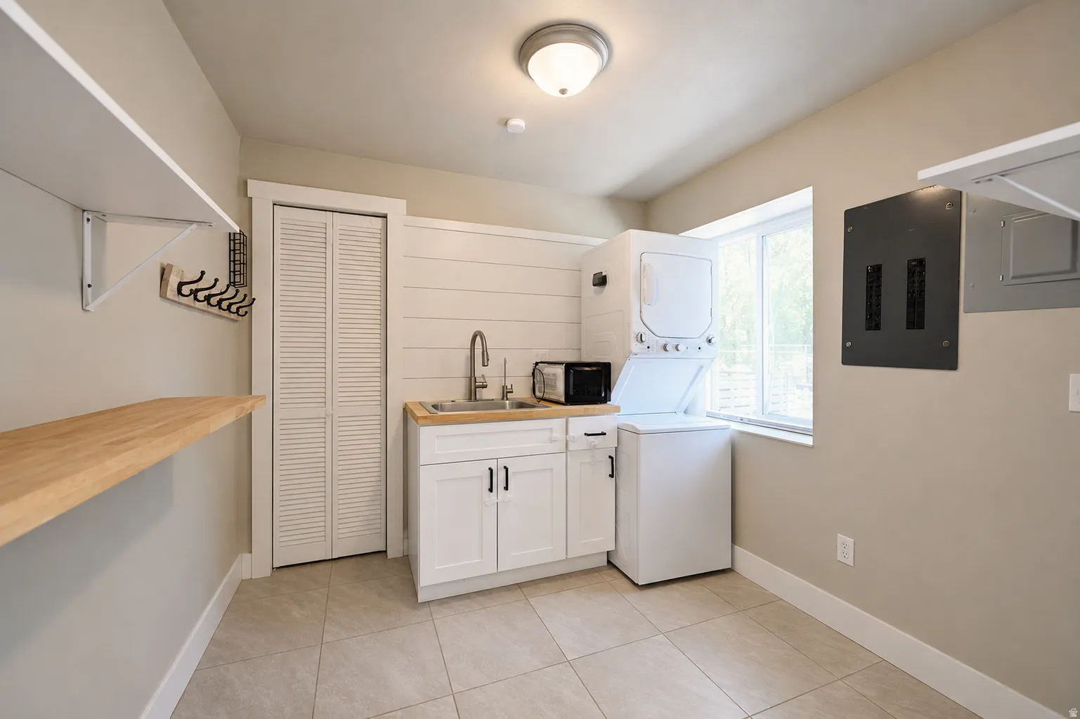 Laundry area featuring a stacked washer and dryer, a utility sink with a wood-finish countertop, white cabinetry with dark hardware, and tiled flooring