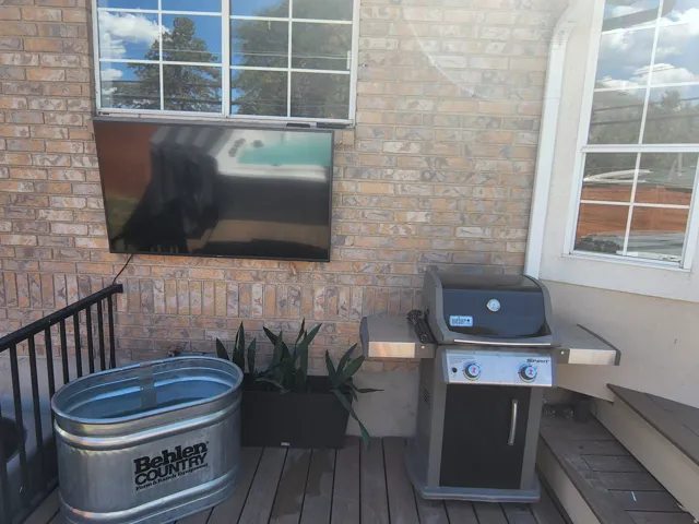 Outdoor entertainment area featuring a mounted television, brick exterior, and wood-finish decking