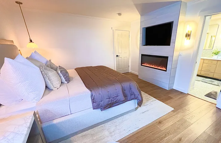 Bedroom featuring wood-finish flooring, a built-in electric fireplace, recessed television niche, and a wall-mounted sconce
