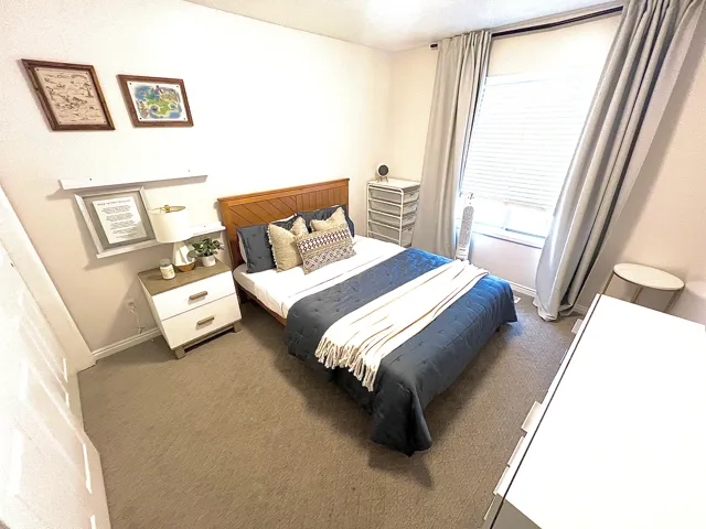 Bedroom featuring a wood-finish headboard, window with blinds and drapes, and a built-in floating shelf