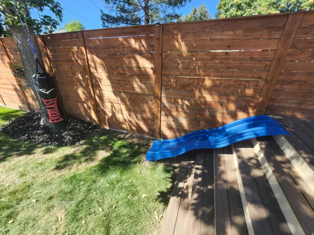 Expansive wood deck with stairs leading to a grassy yard, featuring a privacy fence and mature trees