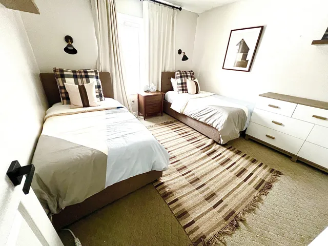 Room featuring two beds with upholstered headboards, sconce lighting, and carpeted flooring
