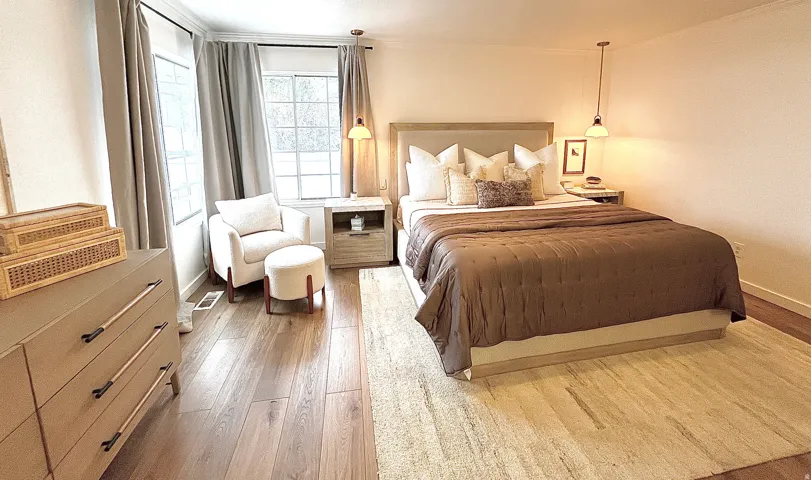 Spacious bedroom with wood-finish flooring, multiple windows, and a neutral color palette
