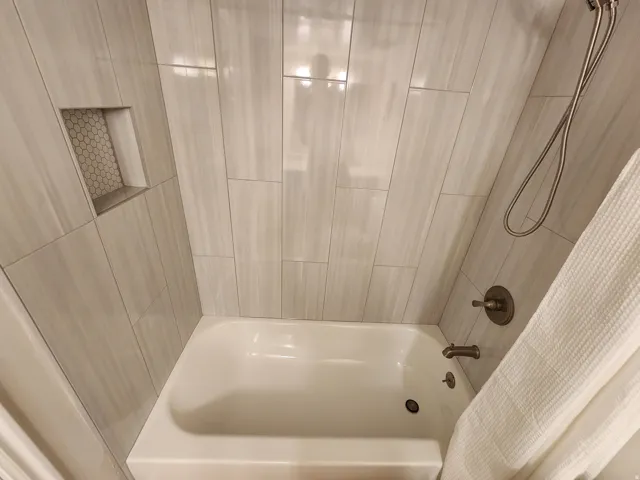Bathtub and shower combination featuring floor-to-ceiling tile surround, a built-in shower niche with mosaic tile, and a handheld showerhead