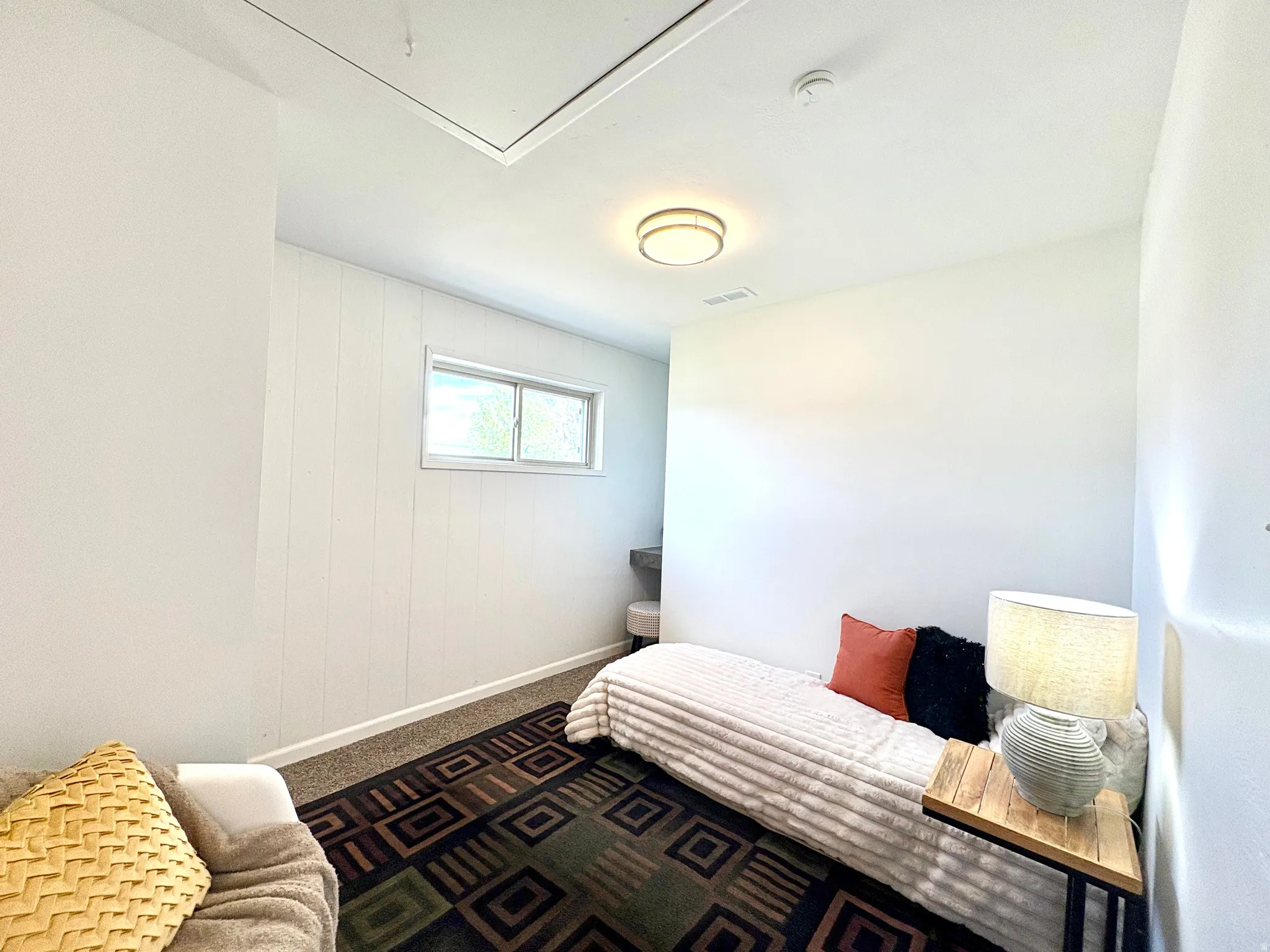 Compact room featuring a single window, overhead flush-mount lighting, wall-to-wall carpeting, and white paneled accent wall
