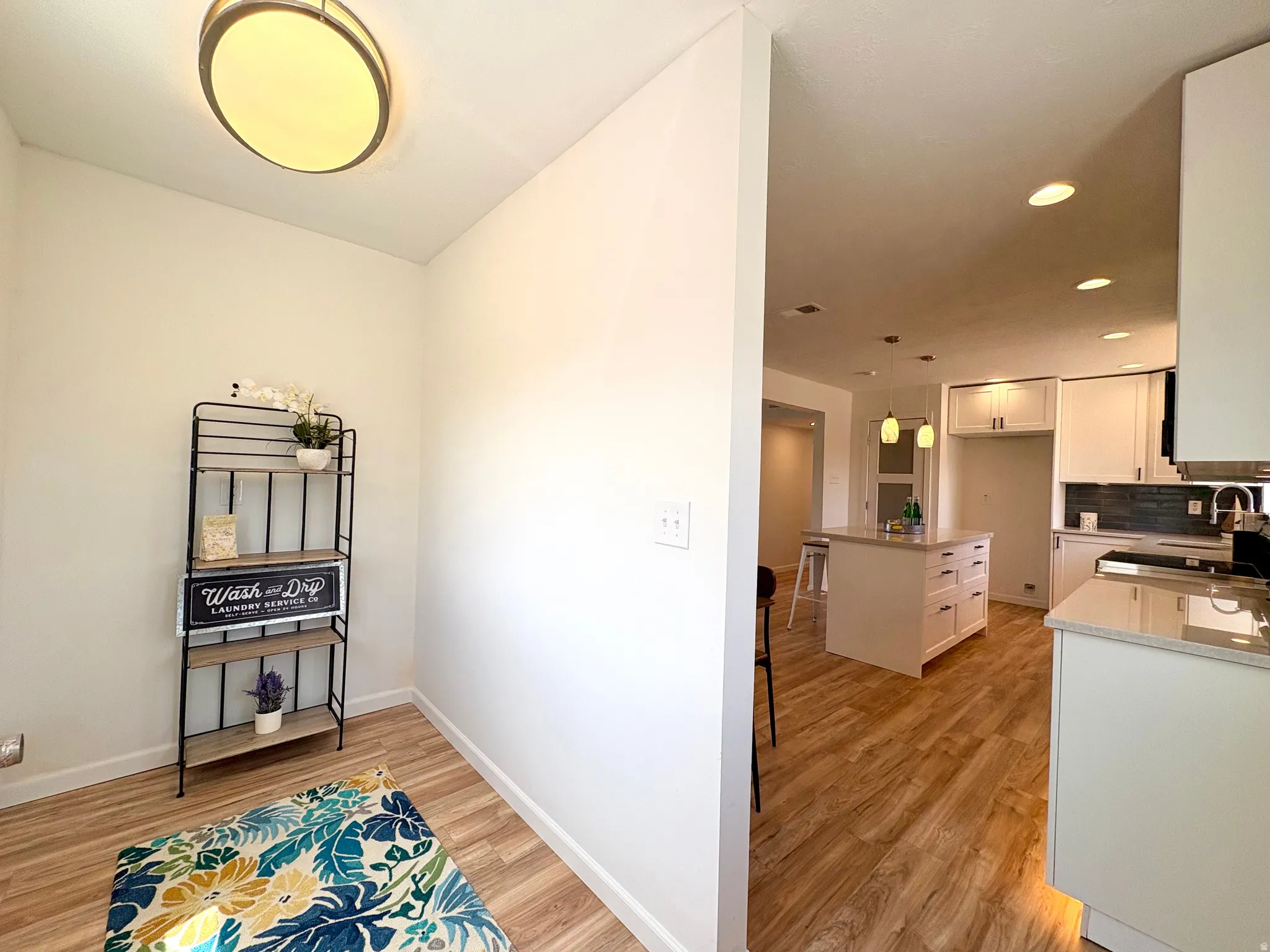 Open-concept kitchen featuring wood-finish flooring, white cabinetry, a central island with storage, recessed lighting, and pendant fixtures