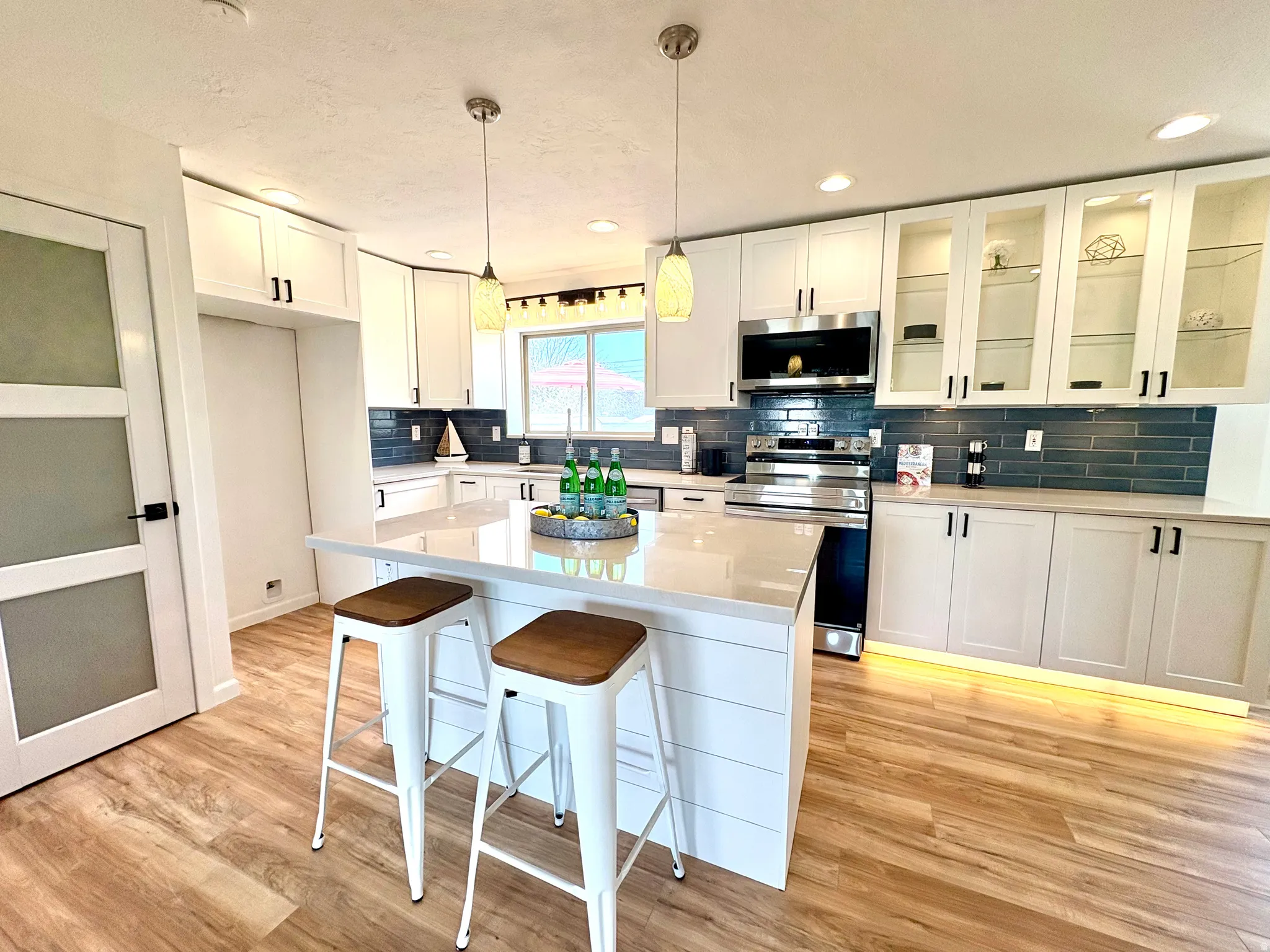 Modern kitchen featuring a central island with shiplap-style paneling, pendant lighting, quartz countertops, a subway tile backsplash, and stainless steel appliances