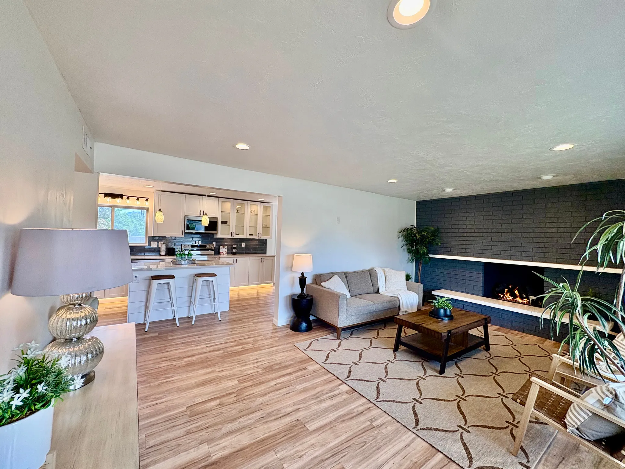Open-concept living area featuring wood-finish flooring, recessed lighting, and a prominent dark brick fireplace with a white mantel