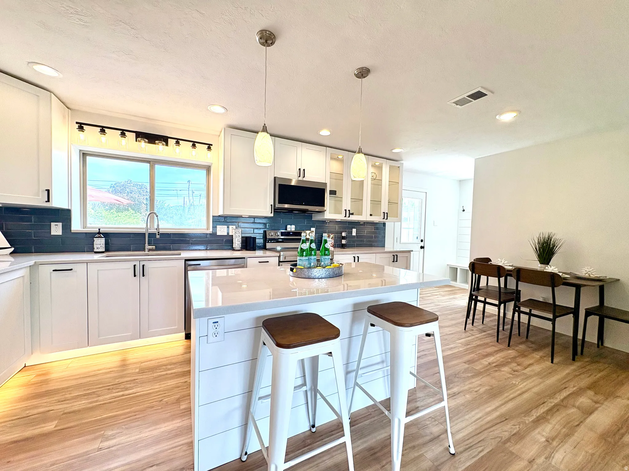 Bright kitchen featuring white shaker cabinetry, an expansive center island with shiplap detailing, quartz countertops, and a subway tile backsplash