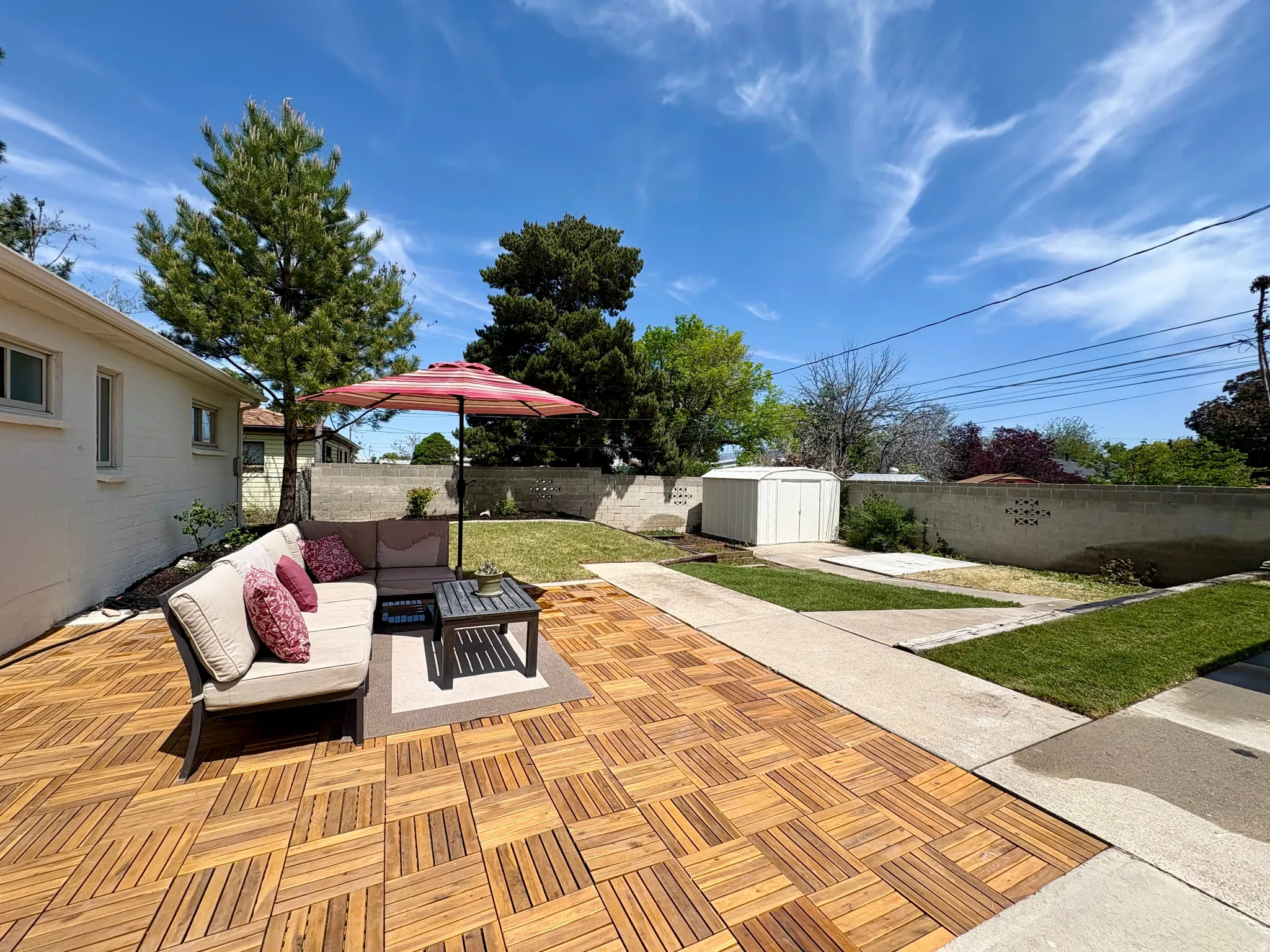 Expansive wood-finish patio featuring a sectional sofa, a dedicated concrete pathway, and a detached storage shed