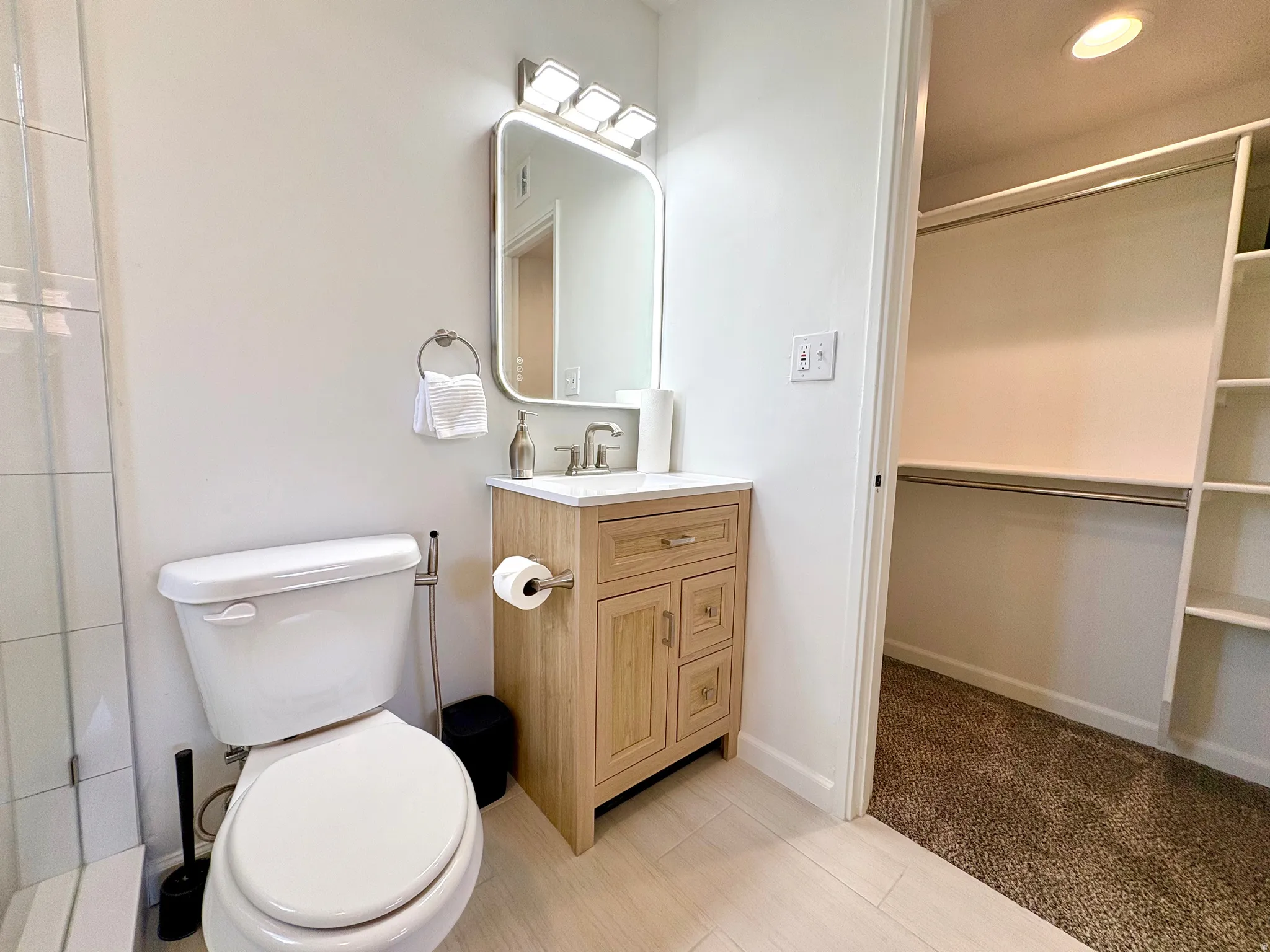 Bathroom with a light wood-finish vanity, white countertop, and rectangular mirror illuminated by a four-bulb fixture