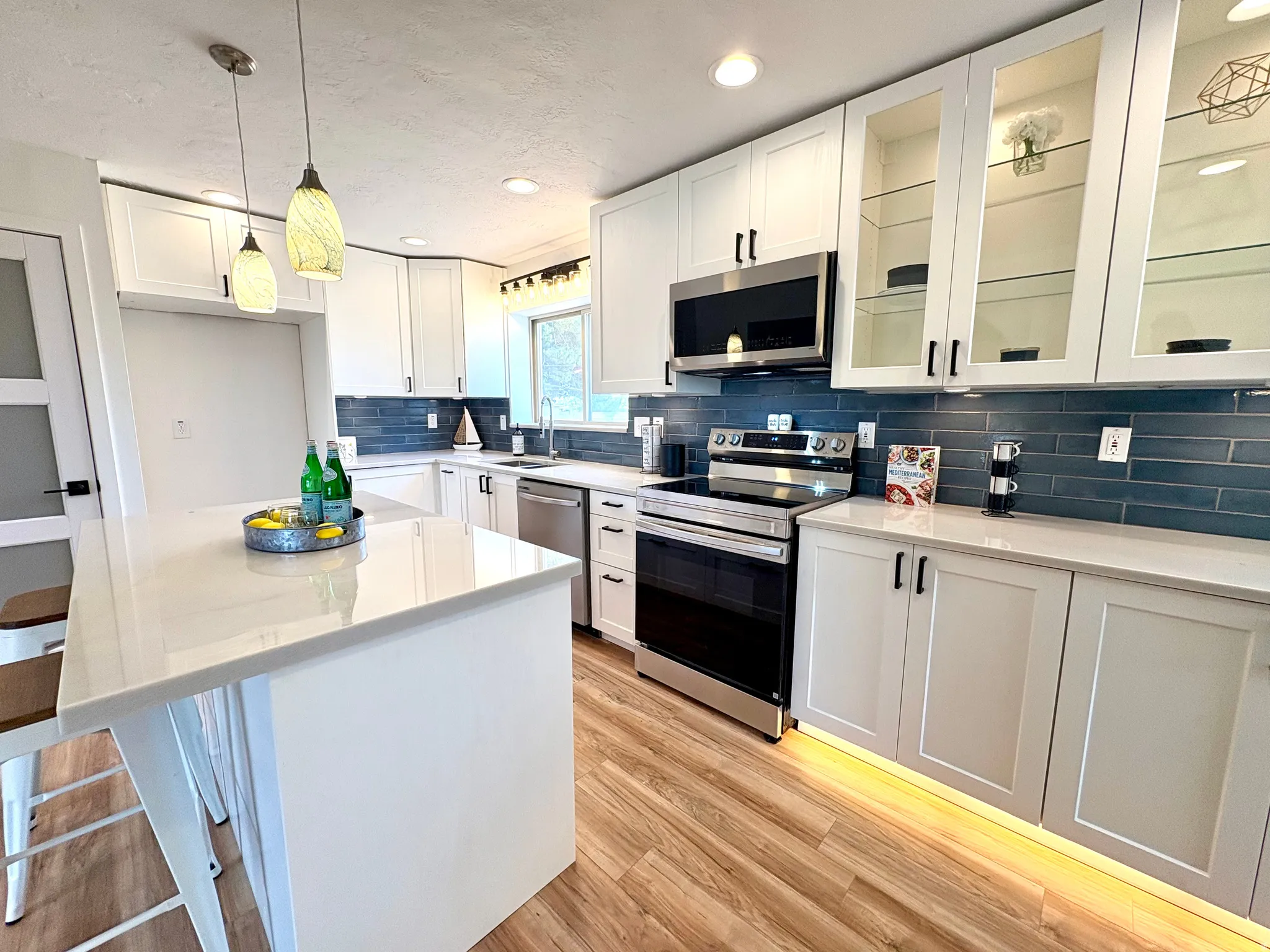 Contemporary kitchen featuring white cabinetry, light-toned countertops, and a blue subway tile backsplash