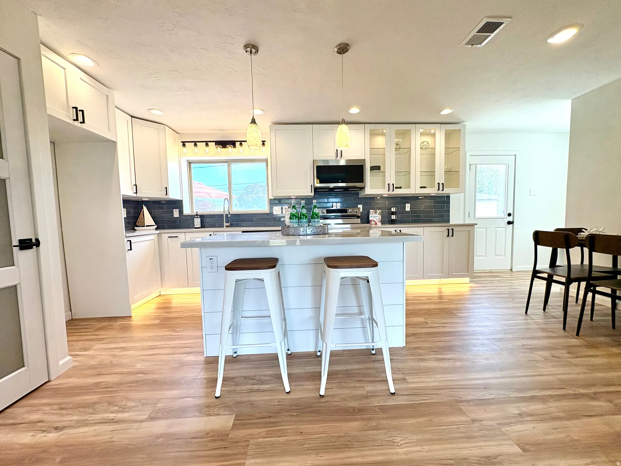Contemporary kitchen featuring white cabinetry, a central island with shiplap detailing, wood-finish flooring, recessed lighting, and stainless steel appliances
