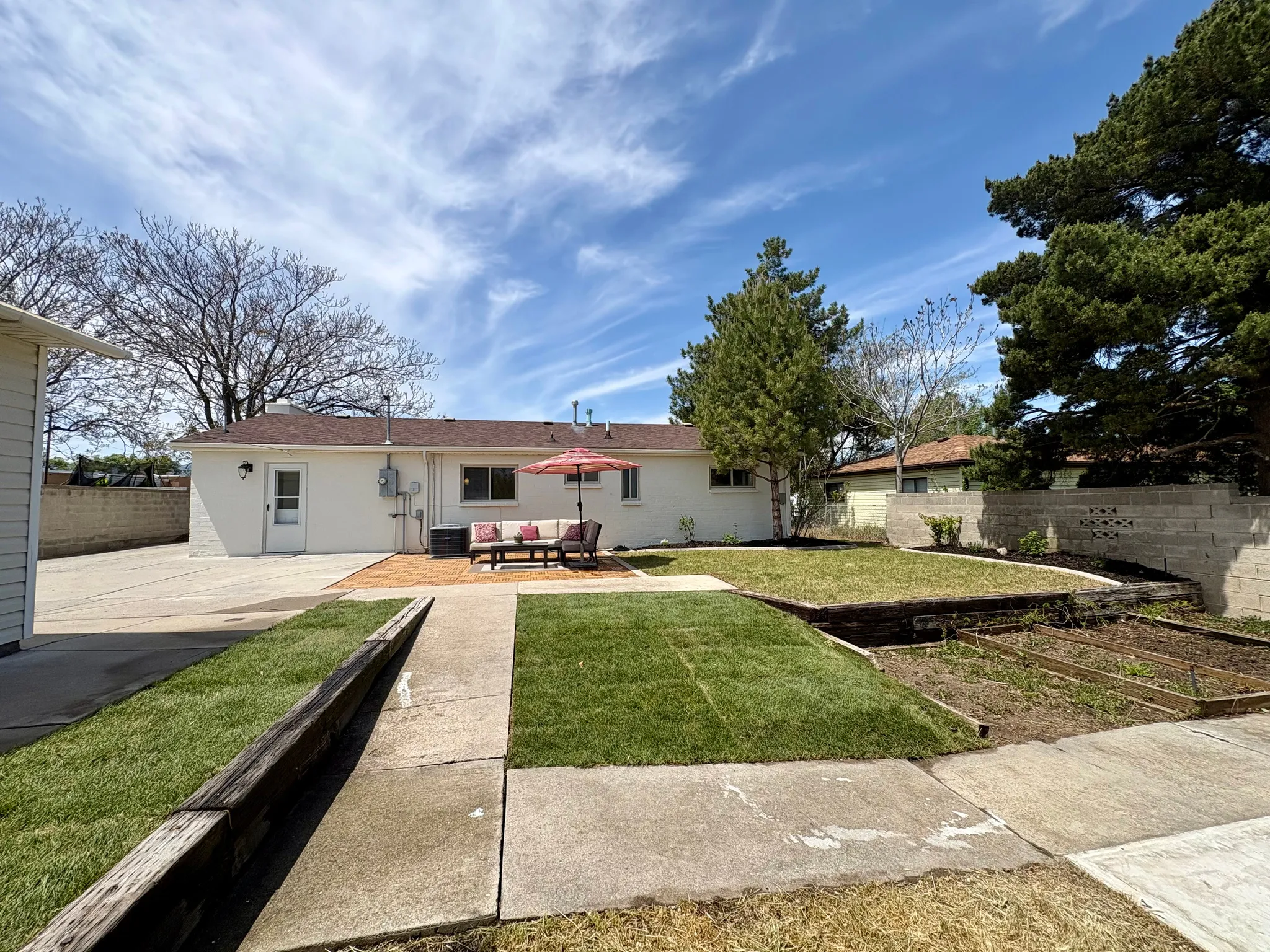 Expansive backyard featuring a brick patio, manicured lawn, and raised garden beds