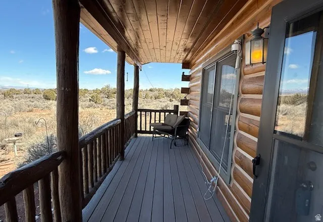 Covered porch featuring log construction, composite decking, a rustic railing, and an exterior wall lantern